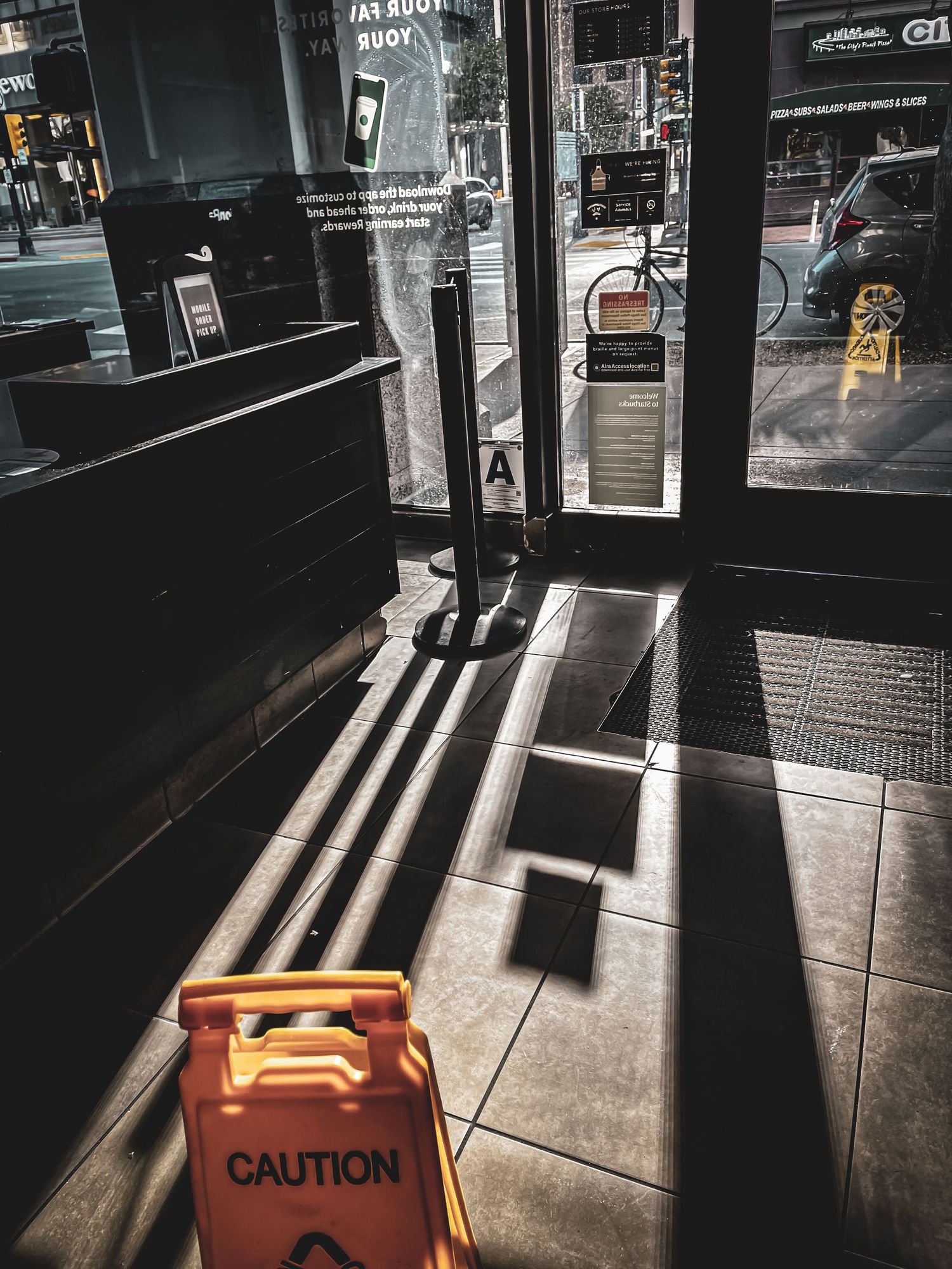 Orange caution sign on floor with dramatic shadows through glass doors.