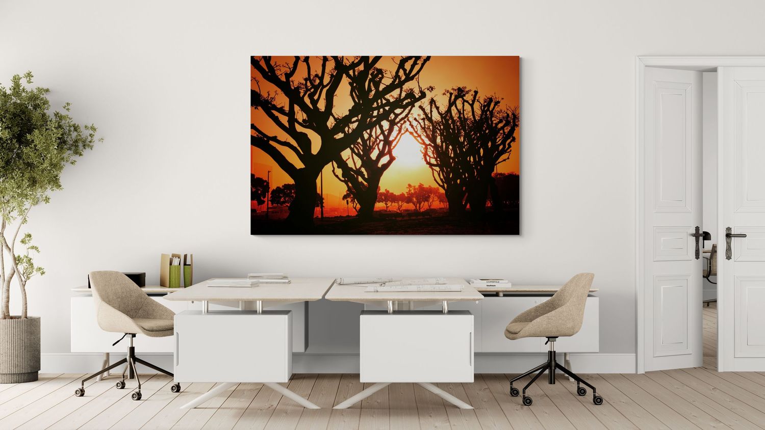 Modern office workspace with white desks and chairs against a wall featuring an orange sunset landscape canvas art print.