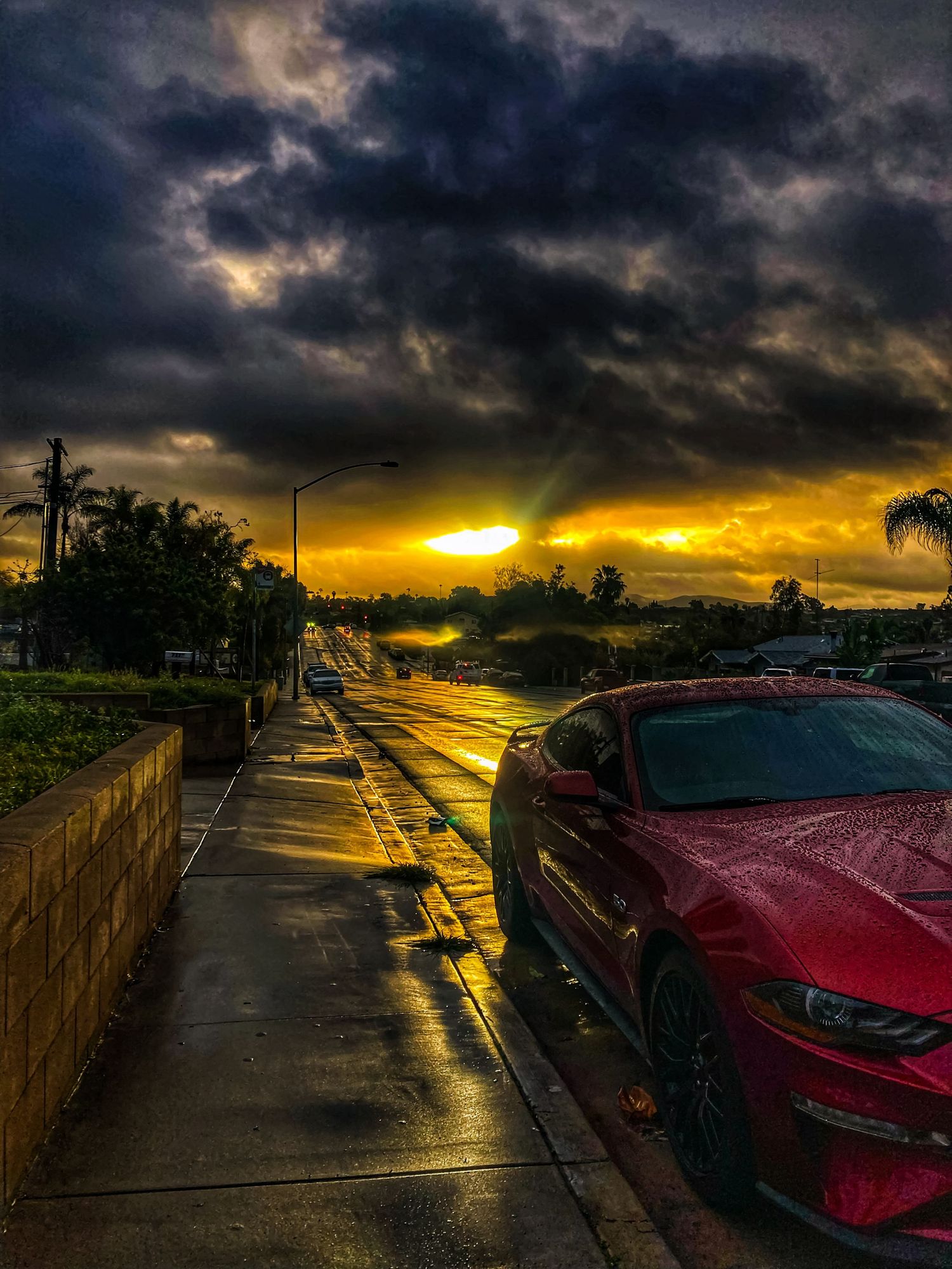 Dramatic sunset sky with dark clouds over wet street and parked red car.