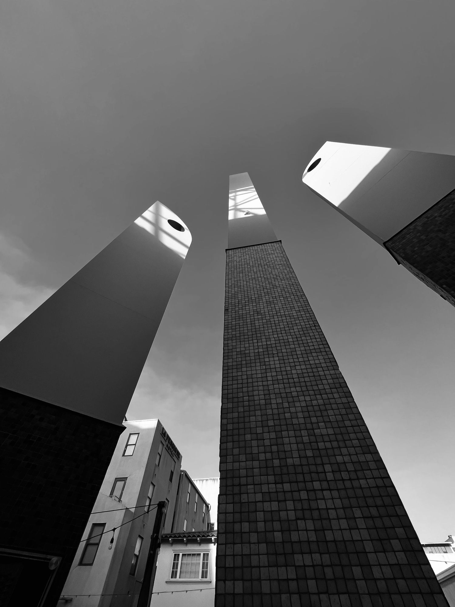 Dramatic upward view of three modern towers against cloudy sky in black and white.