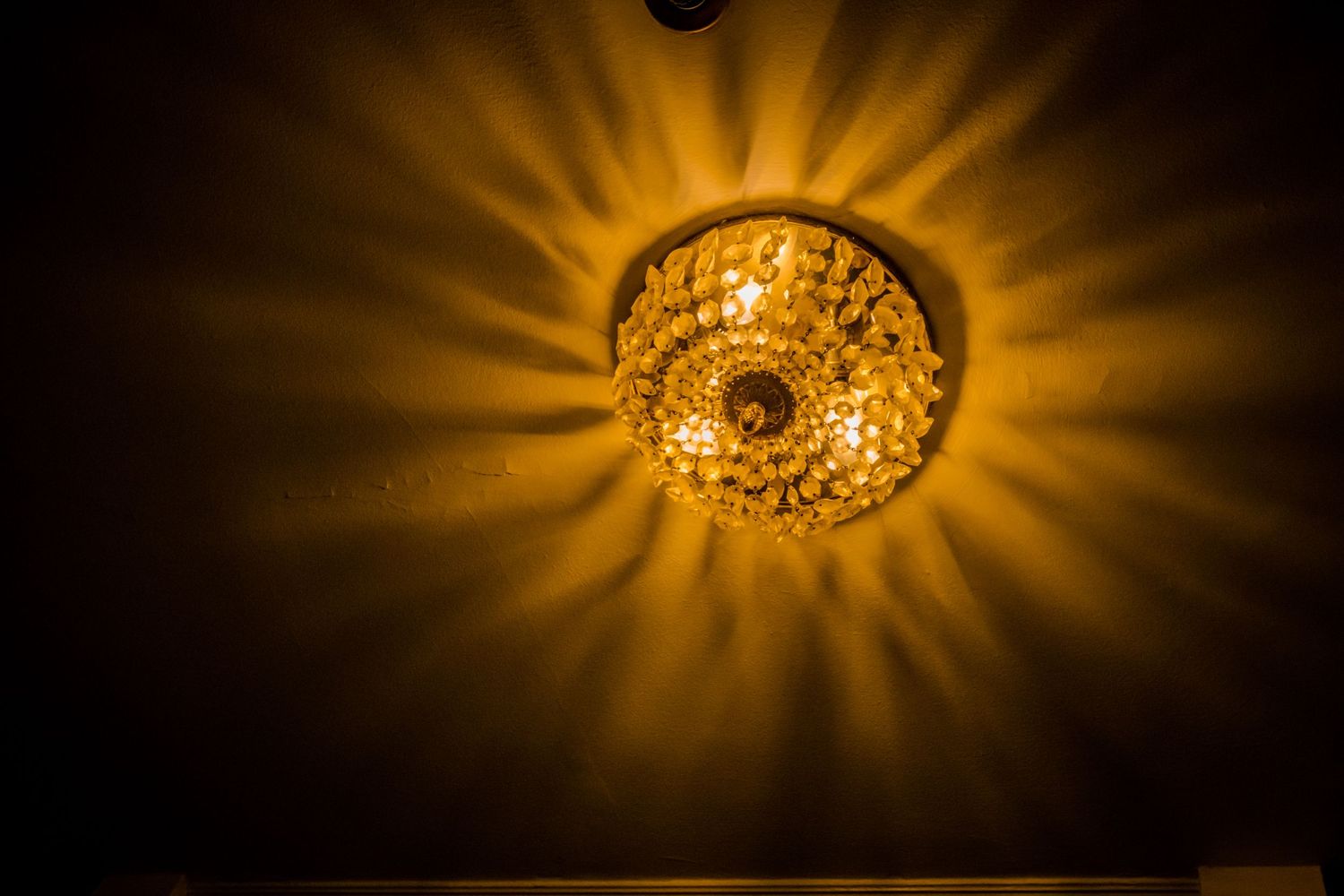 Ornate crystal chandelier casting radiant sunburst pattern of light against dark background.