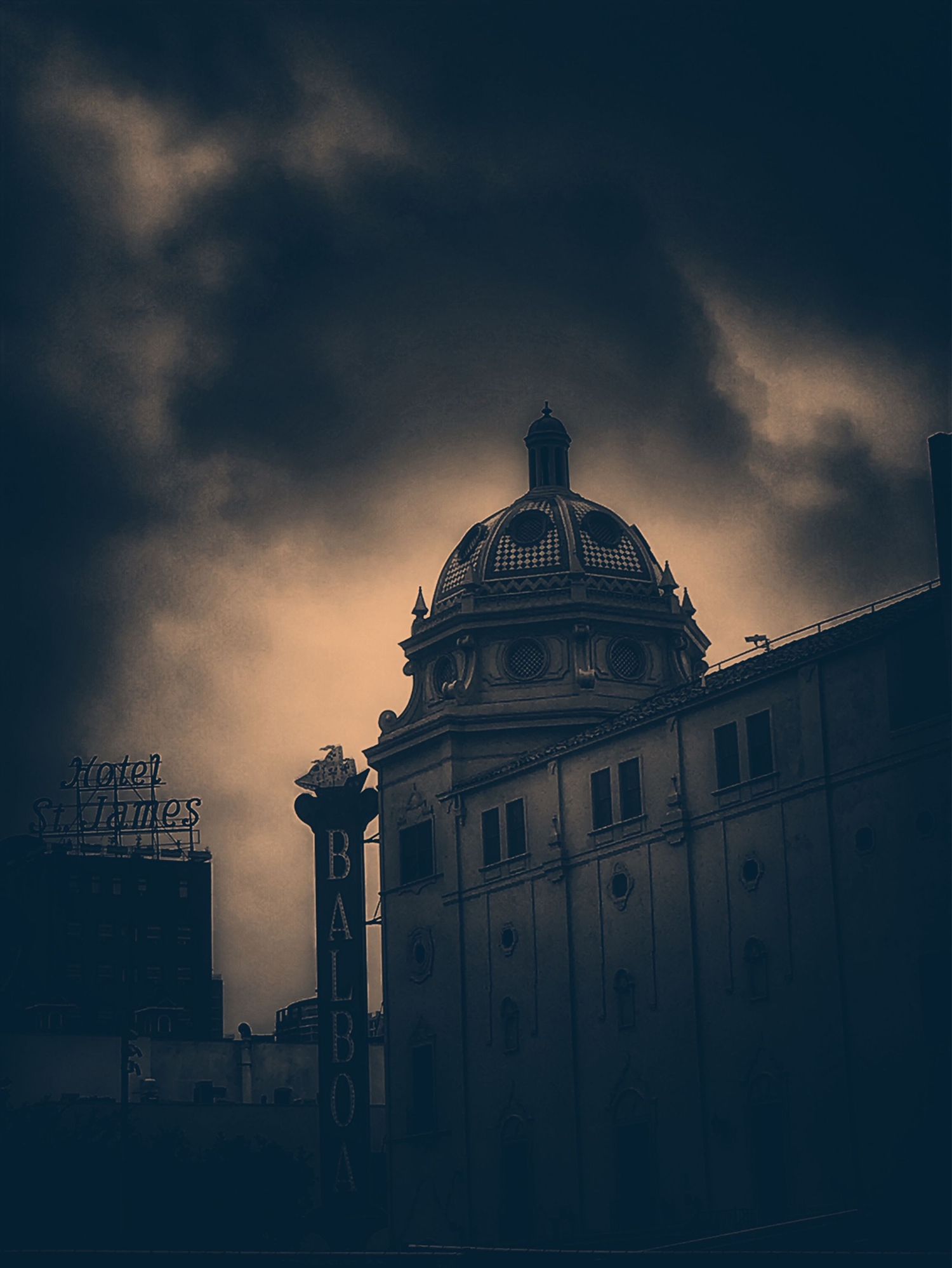 Dramatic silhouette of ornate classical architecture with domed roofs against a moody dark sky at dusk.