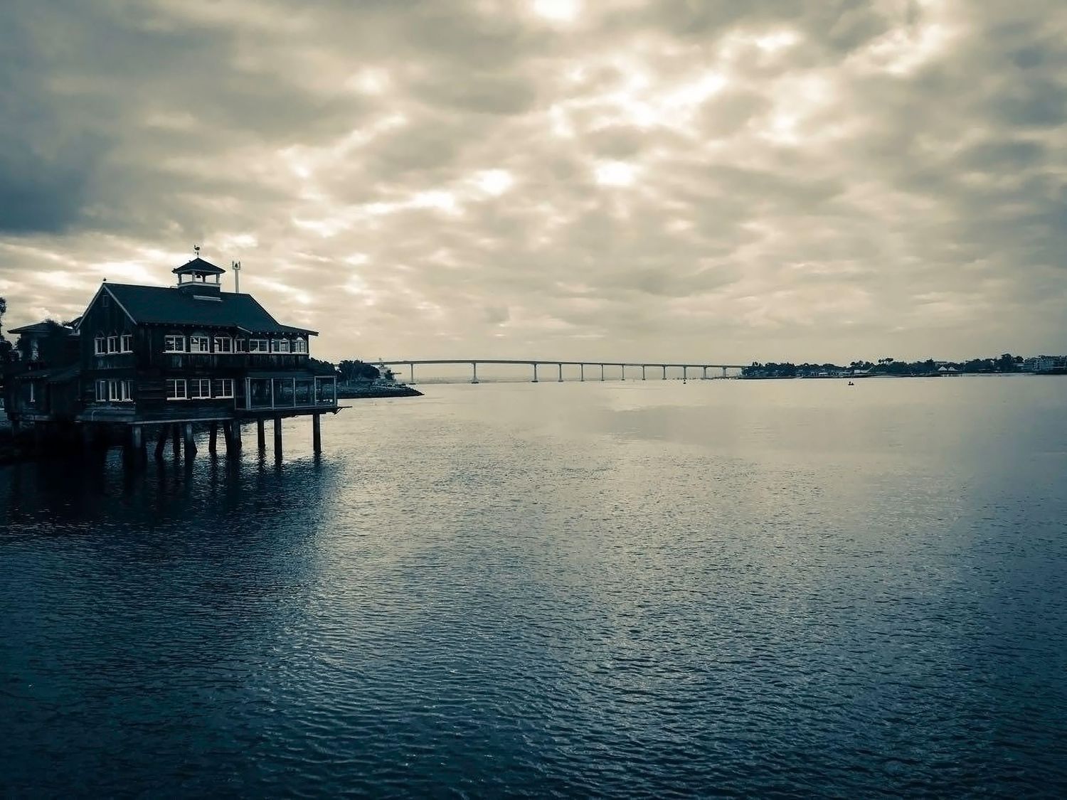 Serene waterfront pier and restaurant overlooking a calm bay with bridge in the distance.