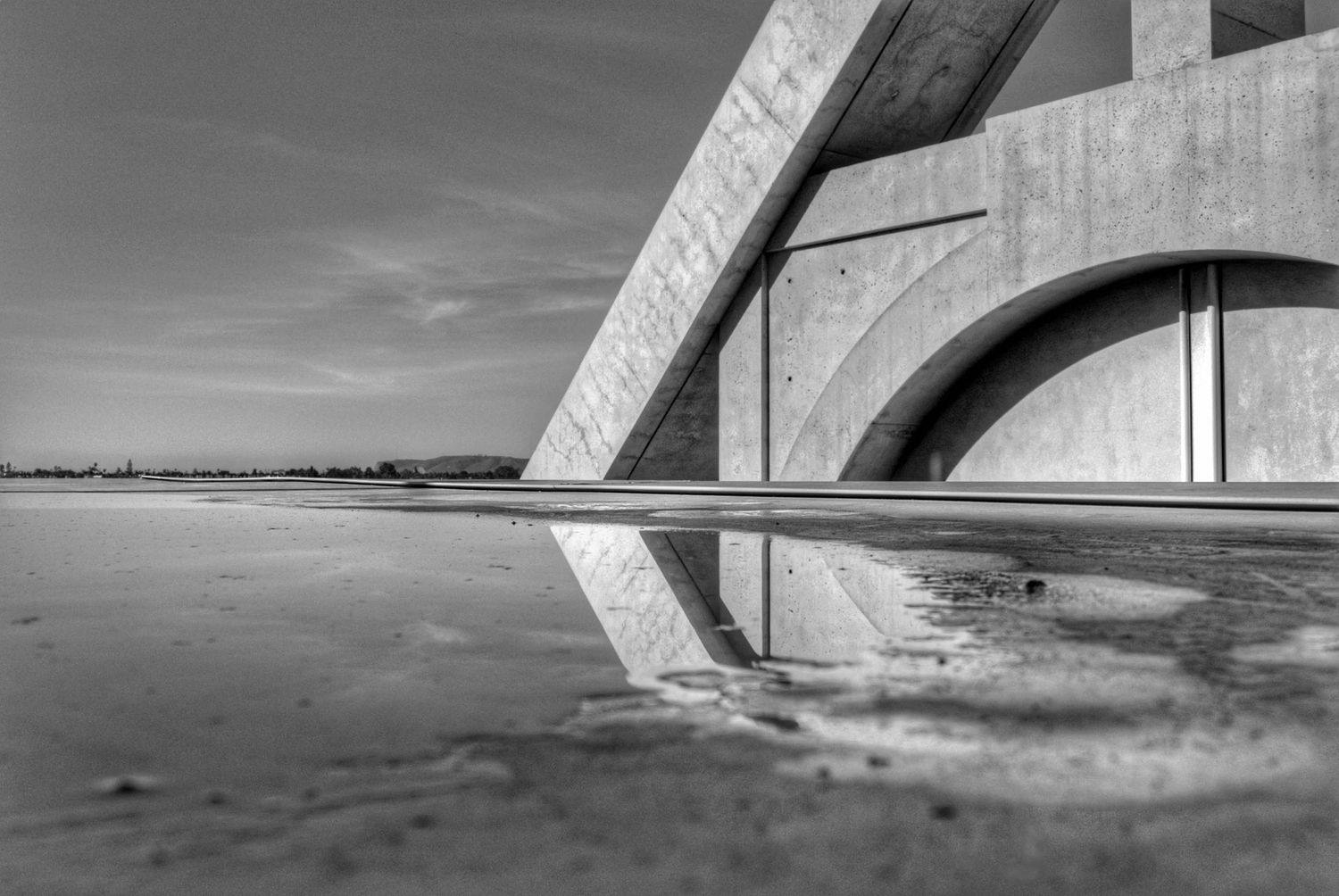Minimalist architectural detail of concrete bridge arch reflected in shallow water.