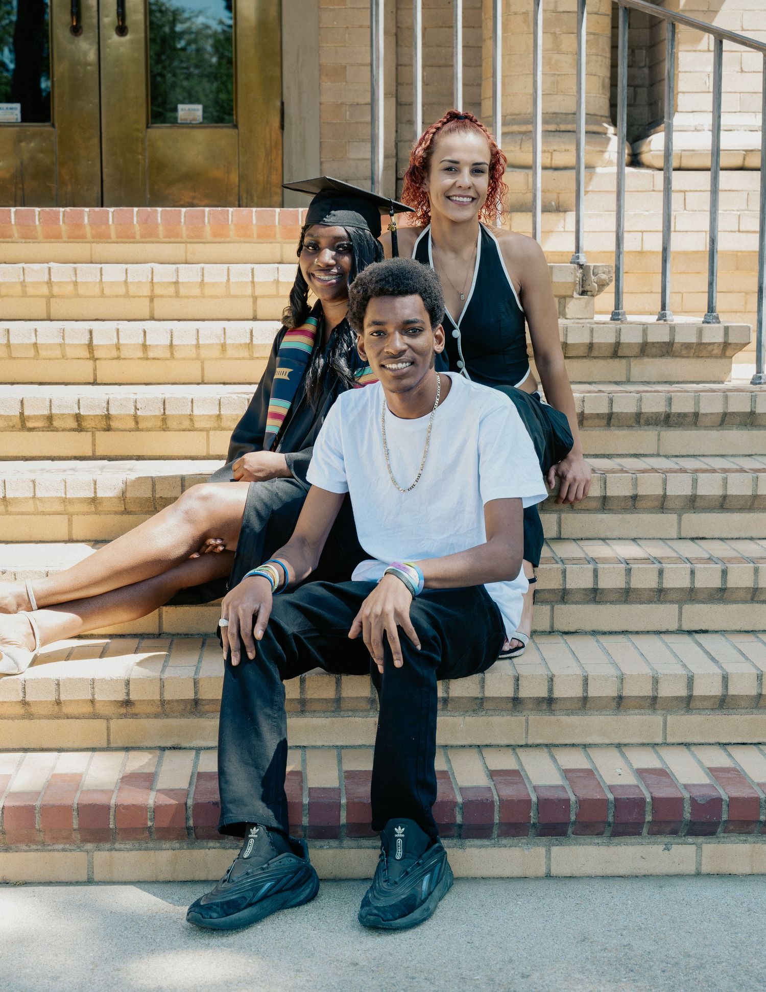 Three people pose on brick steps, one wearing a graduation cap and gown, celebrating a milestone achievement.