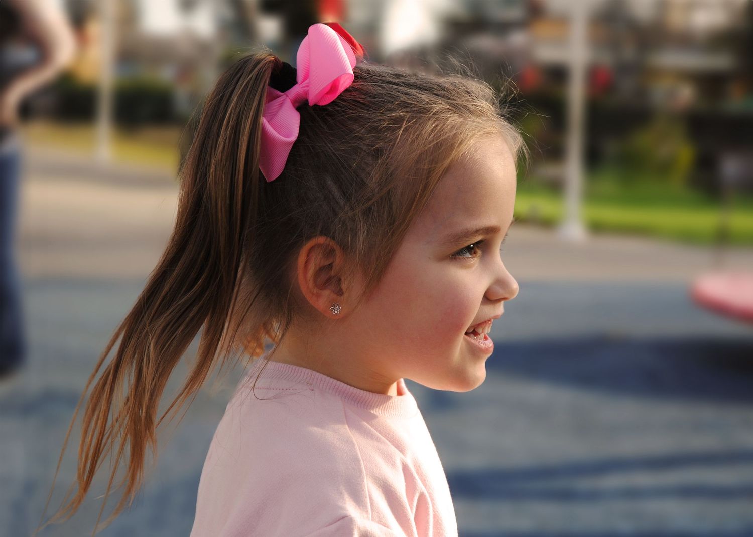 Young girl with a pink bow in her hair smiling in profile view outdoors. Childrens photography by Jolie & Rae Photography Sacramento CA