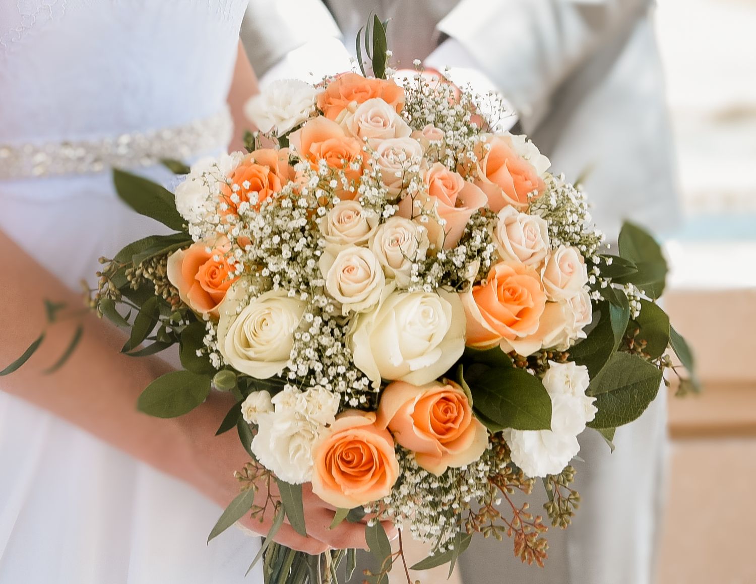 Bridal bouquet close-up with peach and ivory roses, baby's breath, and greenery. Wedding photography detail of romantic floral textures.