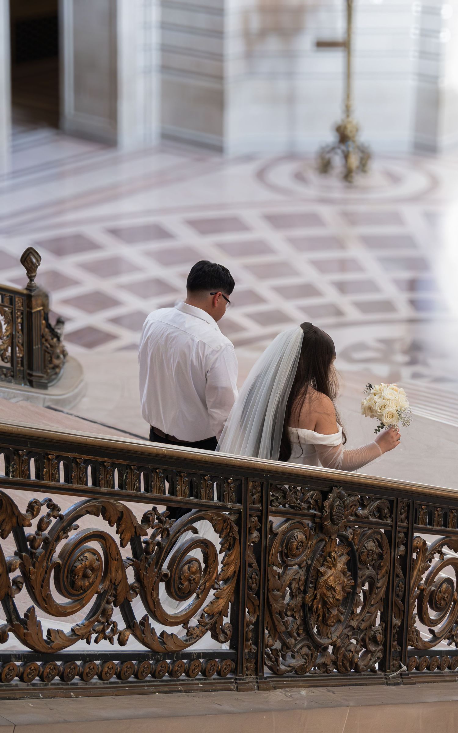 Bride and groom walking down ornate staircase at San Francisco City Hall wedding ceremony.
