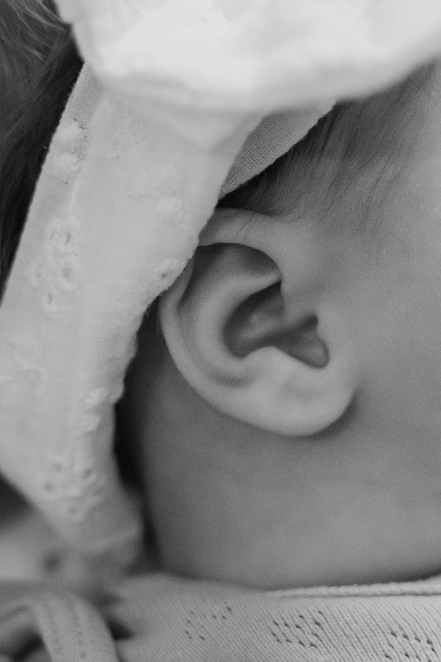 Close-up black and white photo of a newborn baby's delicate ear with a soft lace headband.