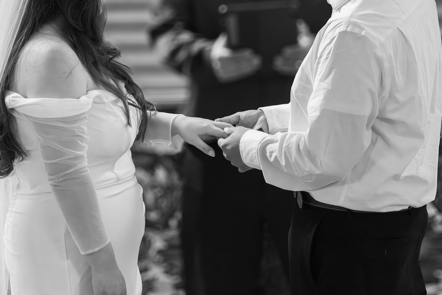 A black and white photo of a couple exchanging rings during their wedding ceremony.