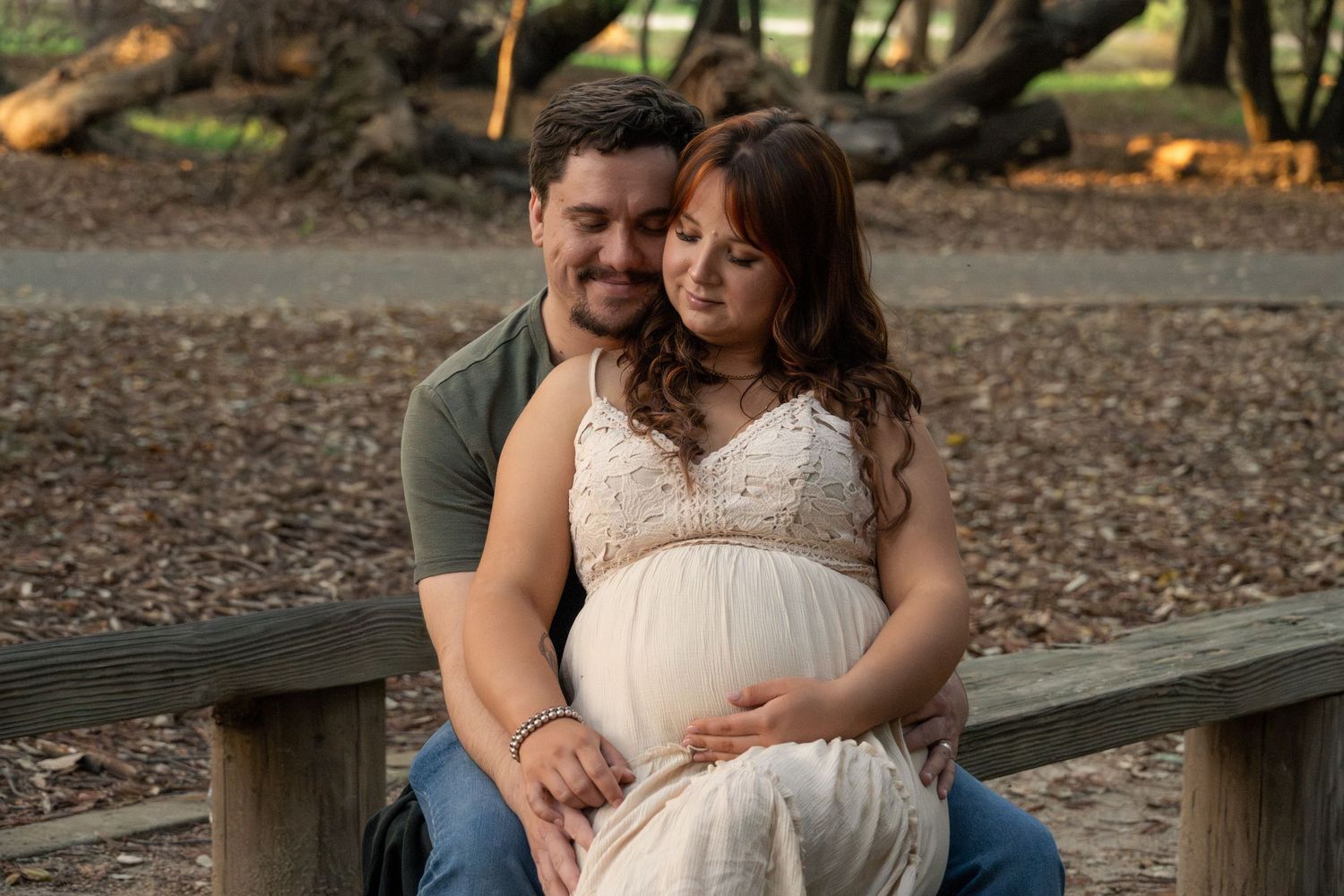 Couple shares intimate moment on wooden bench surrounded by fallen leaves in natural outdoor setting. Tiburon, CA