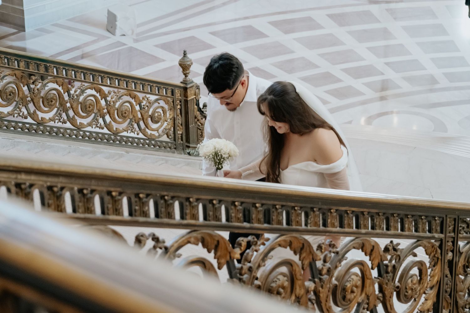 Bride and groom share a romantic moment on an ornate golden staircase railing on a grand staircase in San Francisco City Hall, weddings.