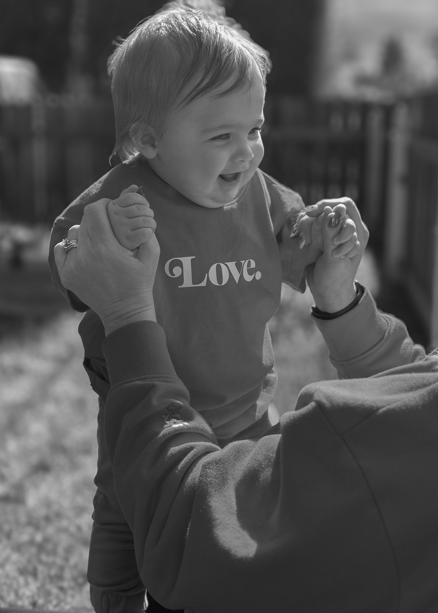 A black and white portrait of a happy baby in a 'Love' sweatshirt reaching forward.
