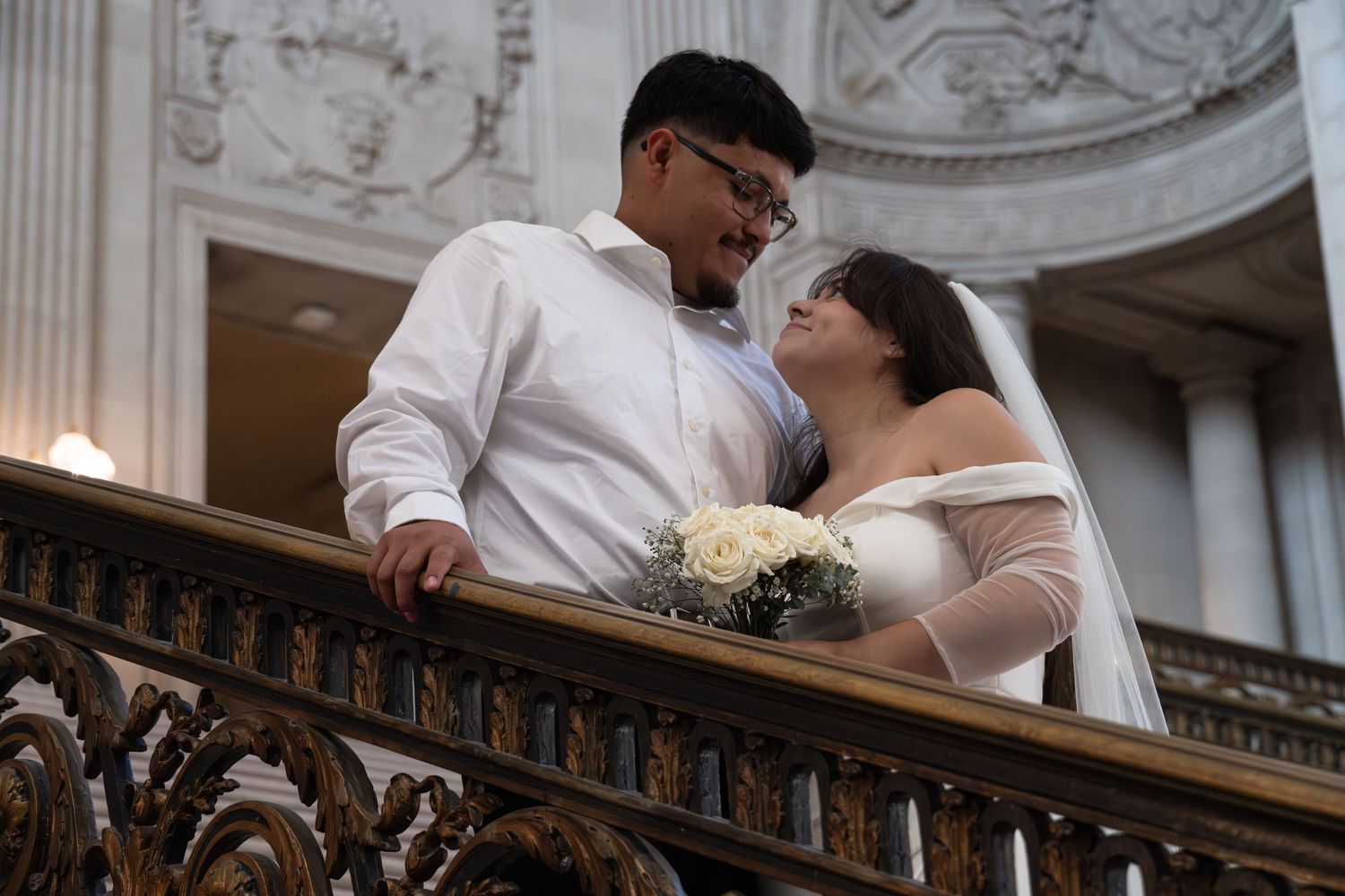 Newlywed couple shares an intimate moment on an ornate marble staircase during their wedding celebration. San Francisco City Hall Photograph
