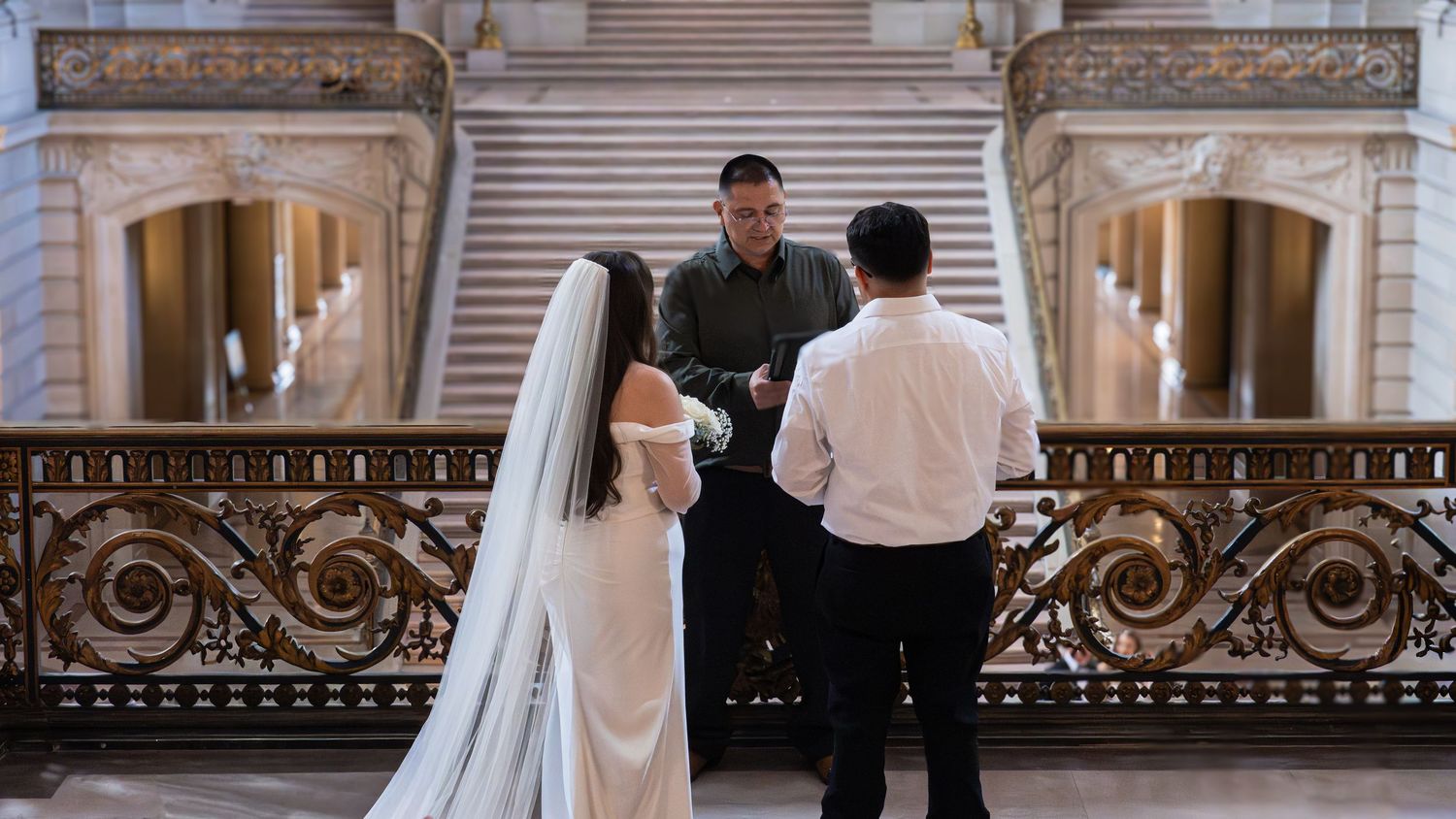 Couple exchanging wedding vows before an officiant at an elegant indoor staircase venue.