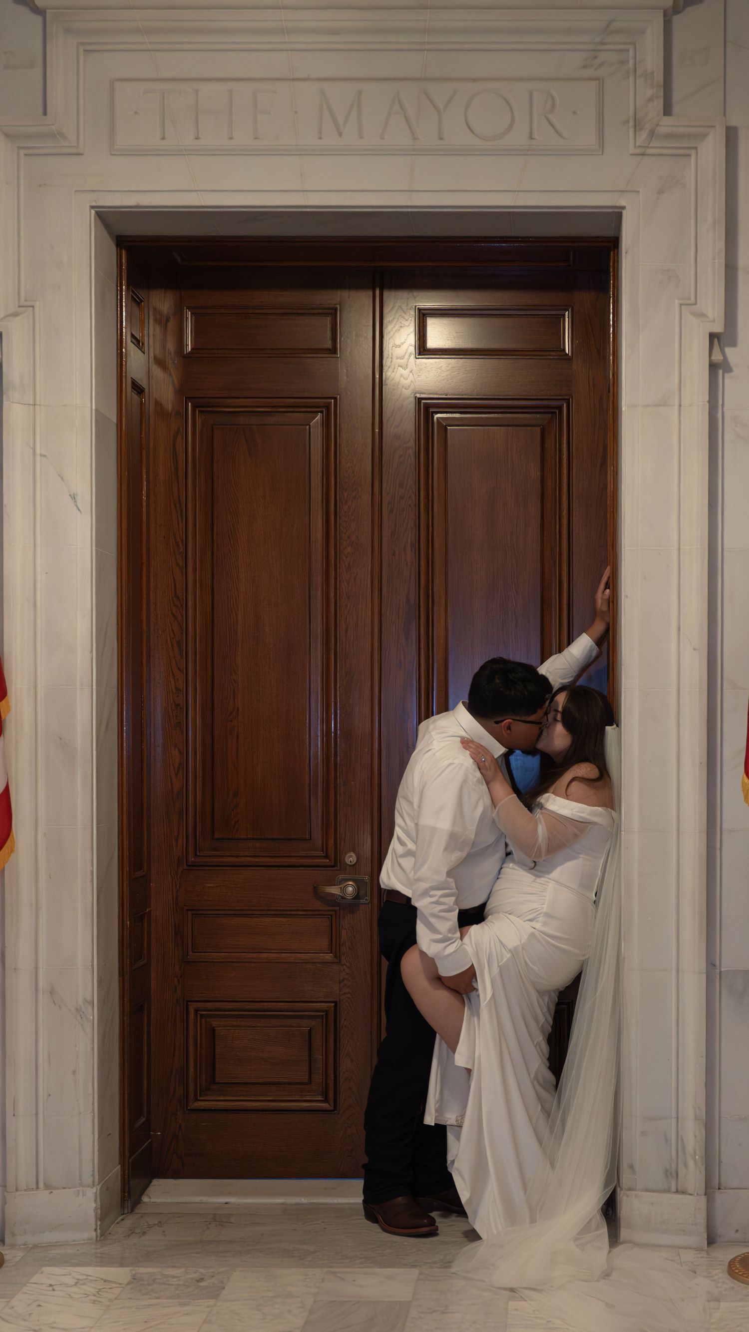 Wedding sequence showing a couple posing playfully by wooden doors marked 'MAYOR'.