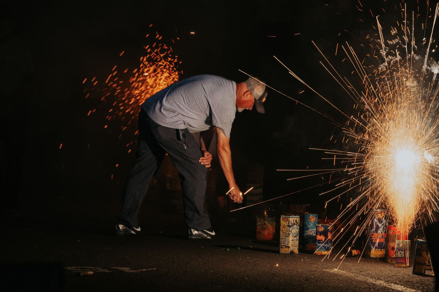 A person lighting fireworks at night with sparks flying dramatically in the darkness.