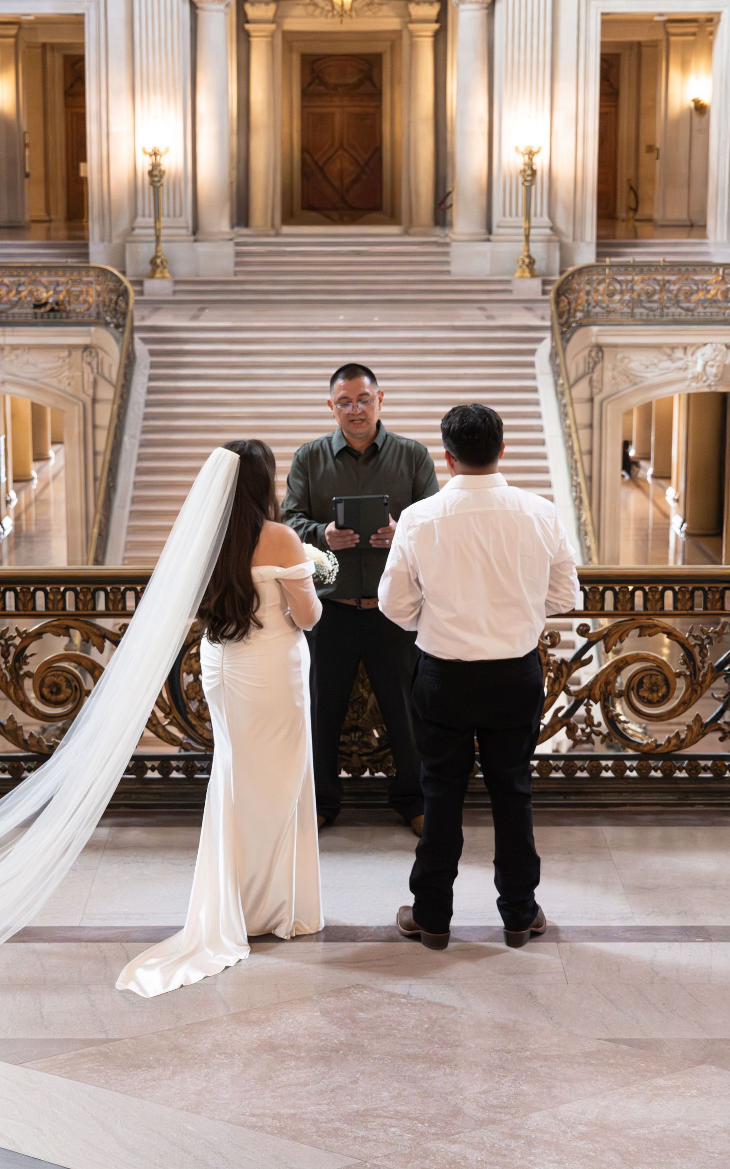 Bride and groom exchange vows with officiant at San Francisco City Hall grand staircase wedding ceremony.