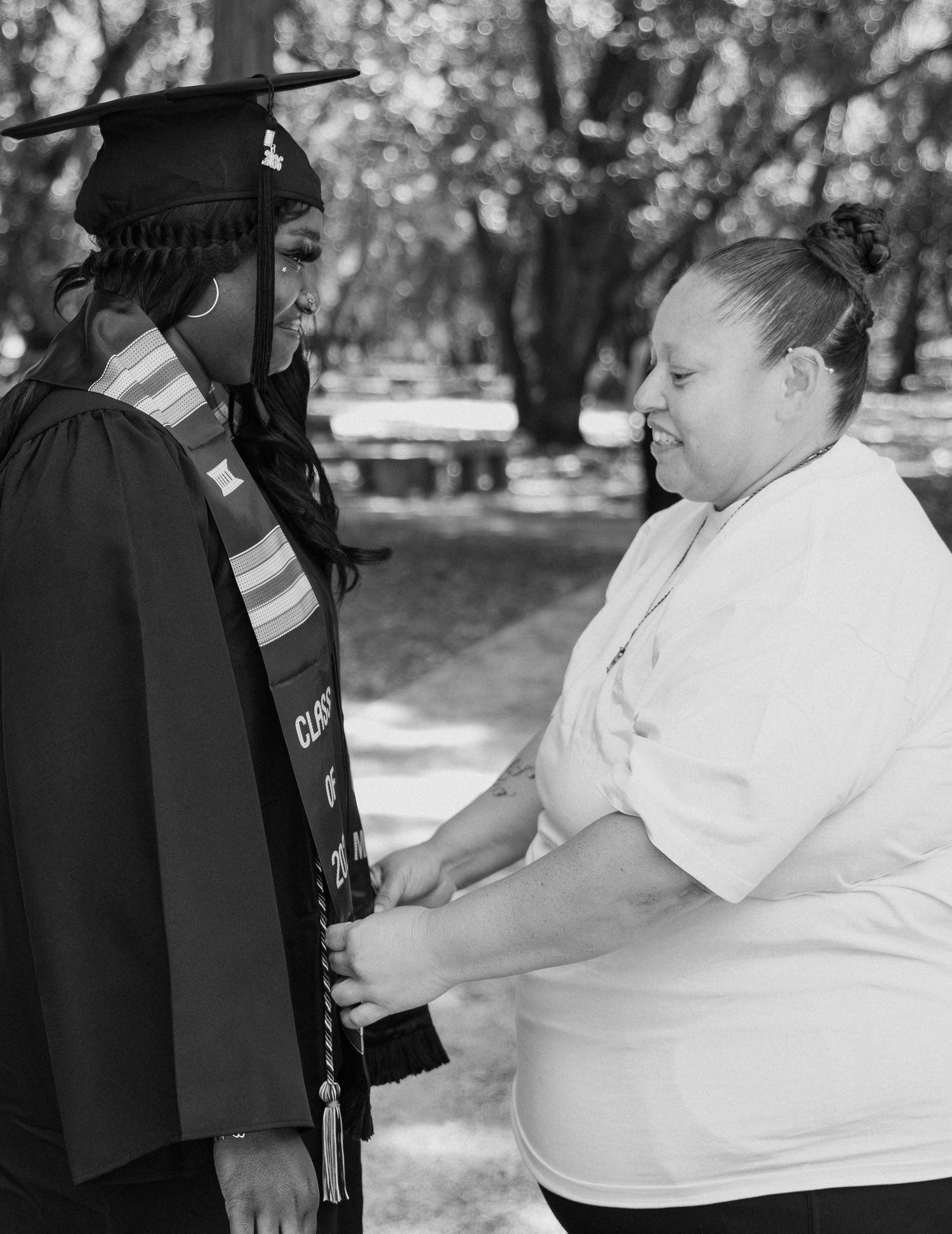 Black and white photo of a graduate in cap and gown sharing a proud moment with a loved one outdoors.
