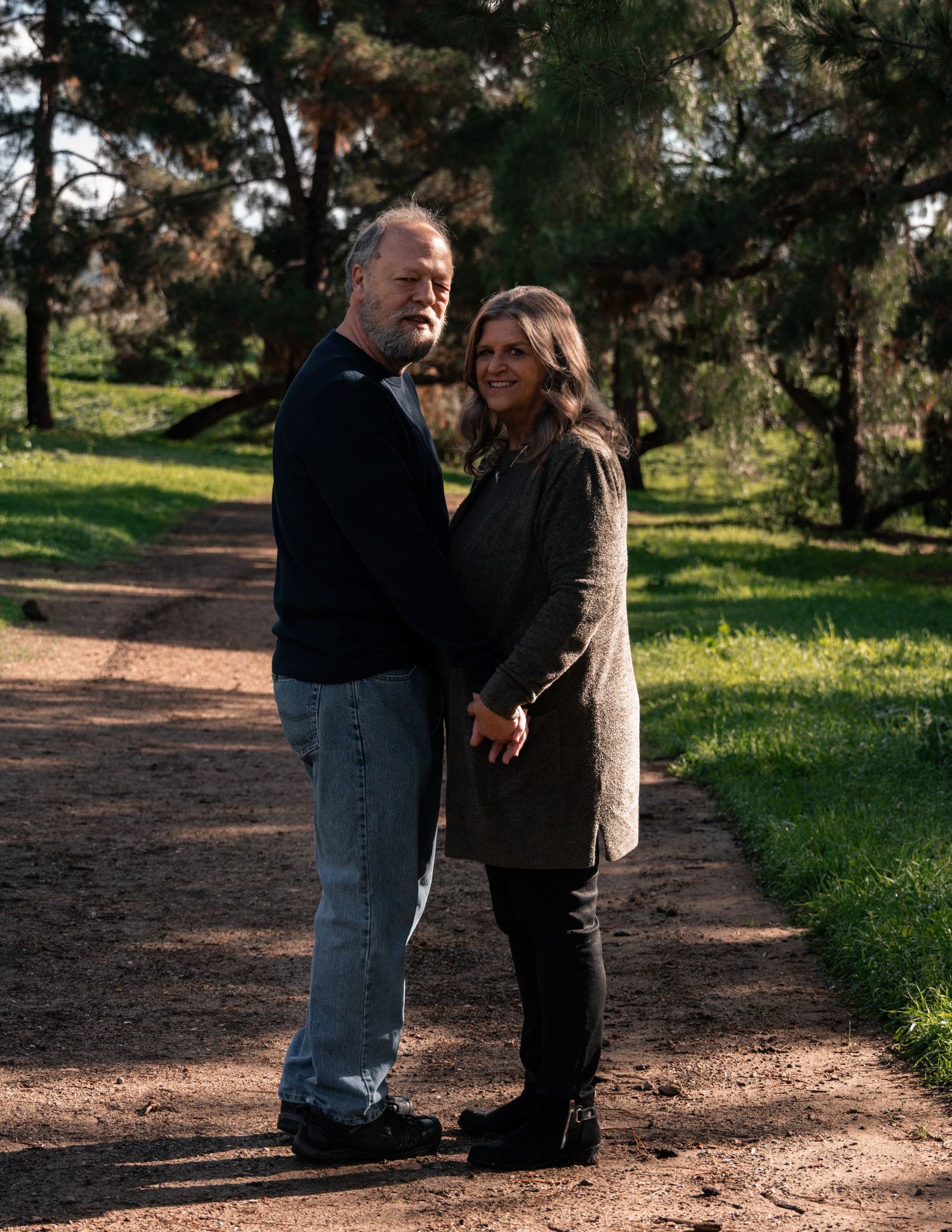 A couple walks together on a dirt path surrounded by trees and grass.