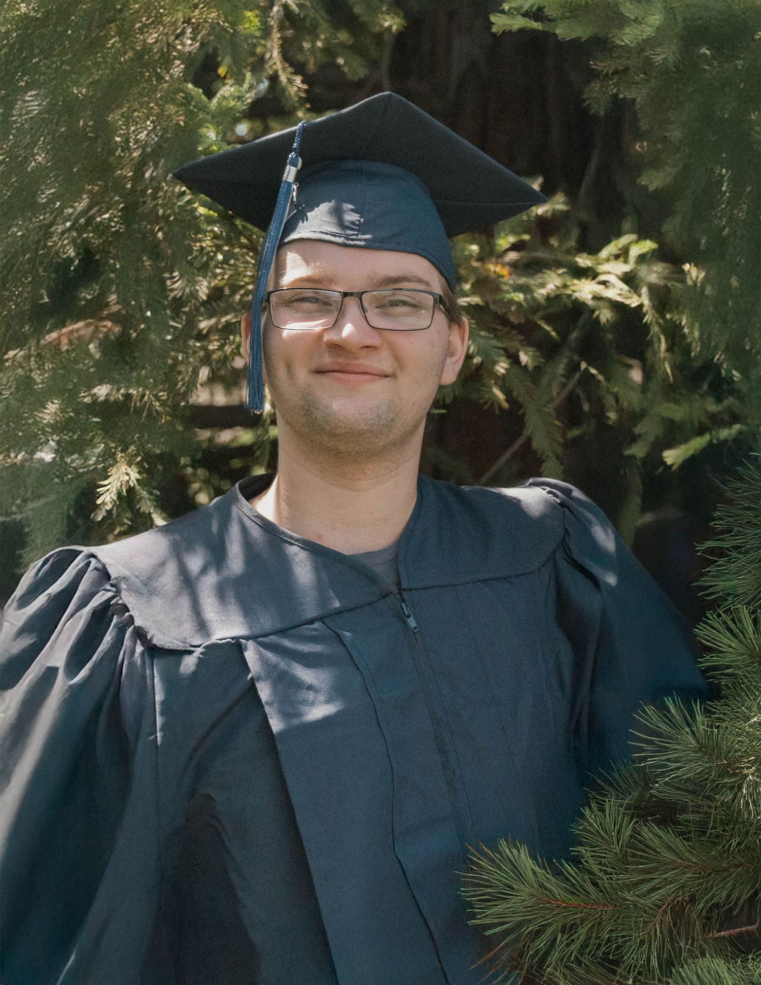 Male graduate in navy cap and gown outdoors with native foliage, senior portrait session, Jolie & Rae Photography Sacramento California
