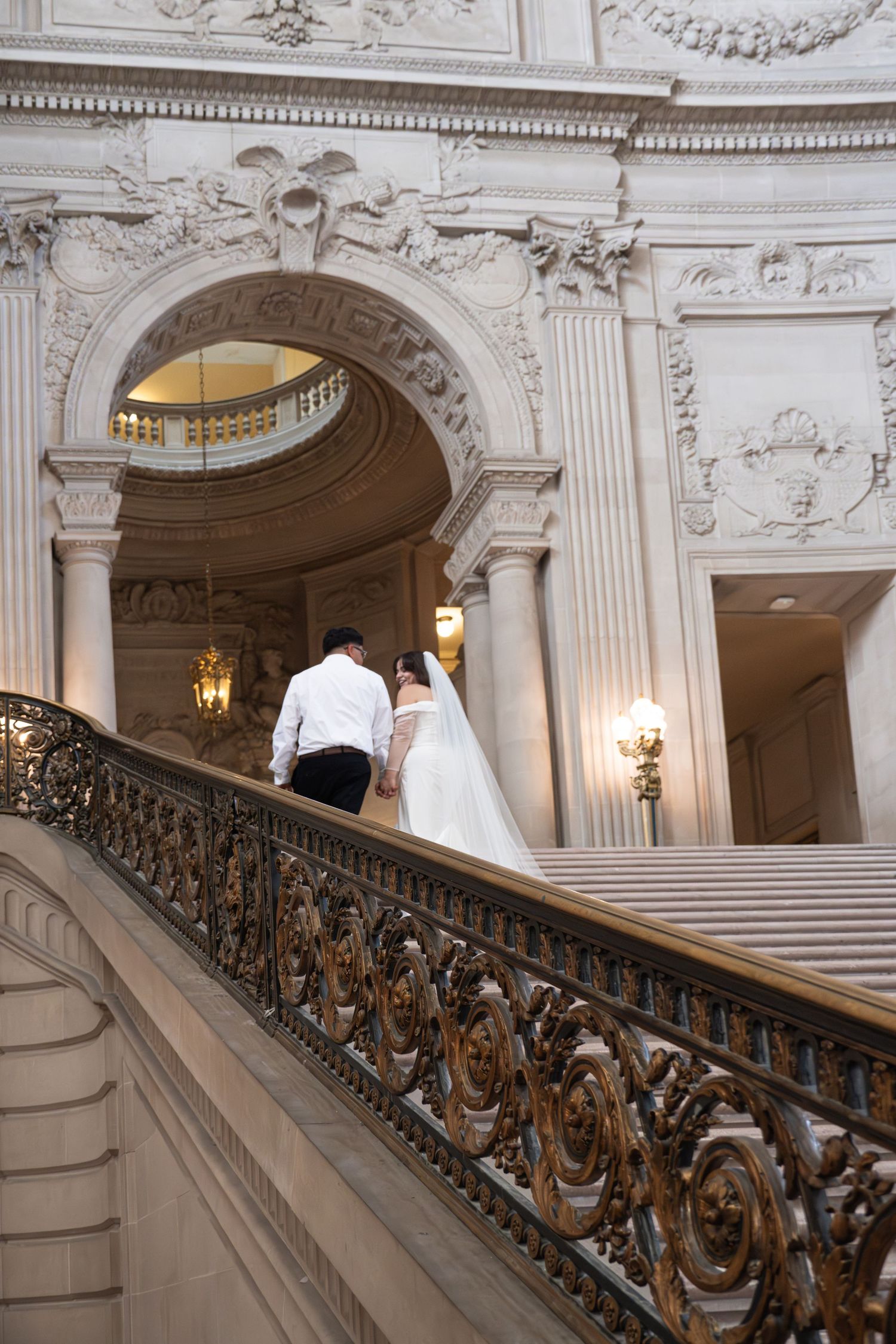 Bride and groom walk up ornate grand staircase at San Francisco City Hall on their wedding day.