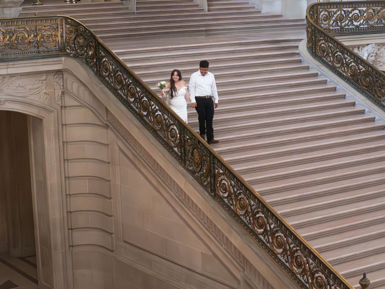 Elegant marble staircase with ornate bronze railings in a historic building interior.