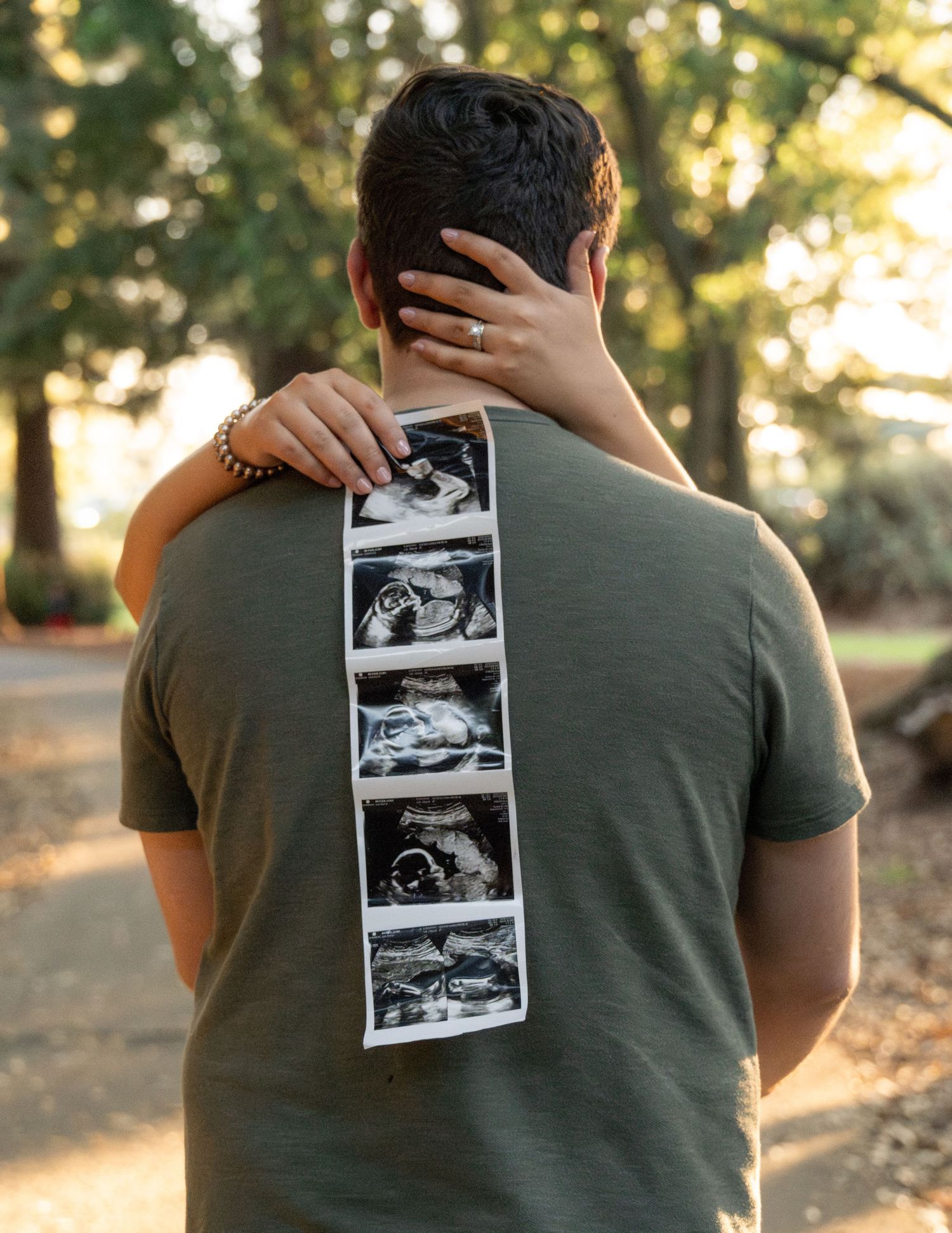 Person in green shirt holds black and white ultrasound photos outdoors during golden hour sunset.