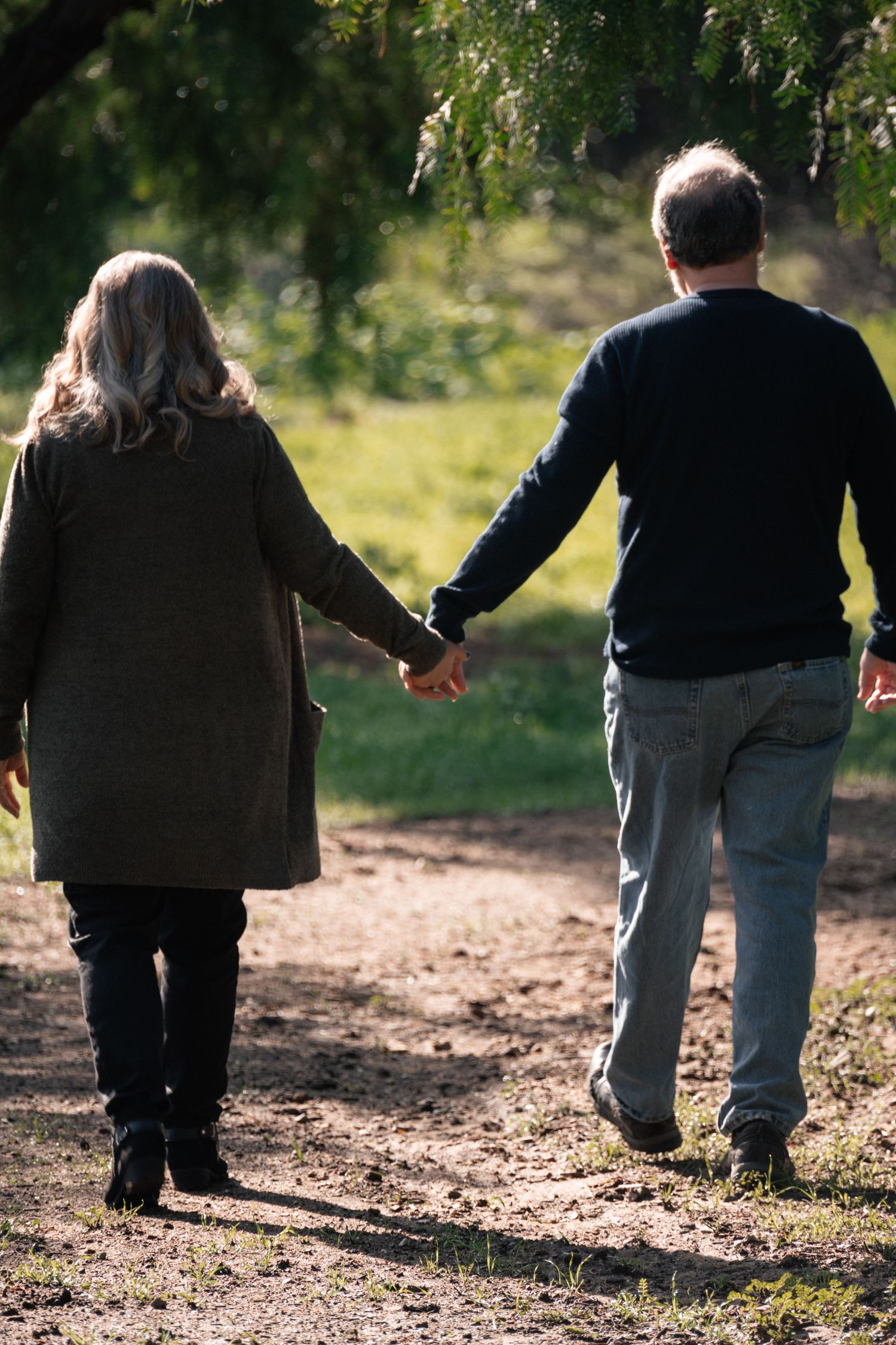 Couple walking together on a sunlit dirt path through trees.