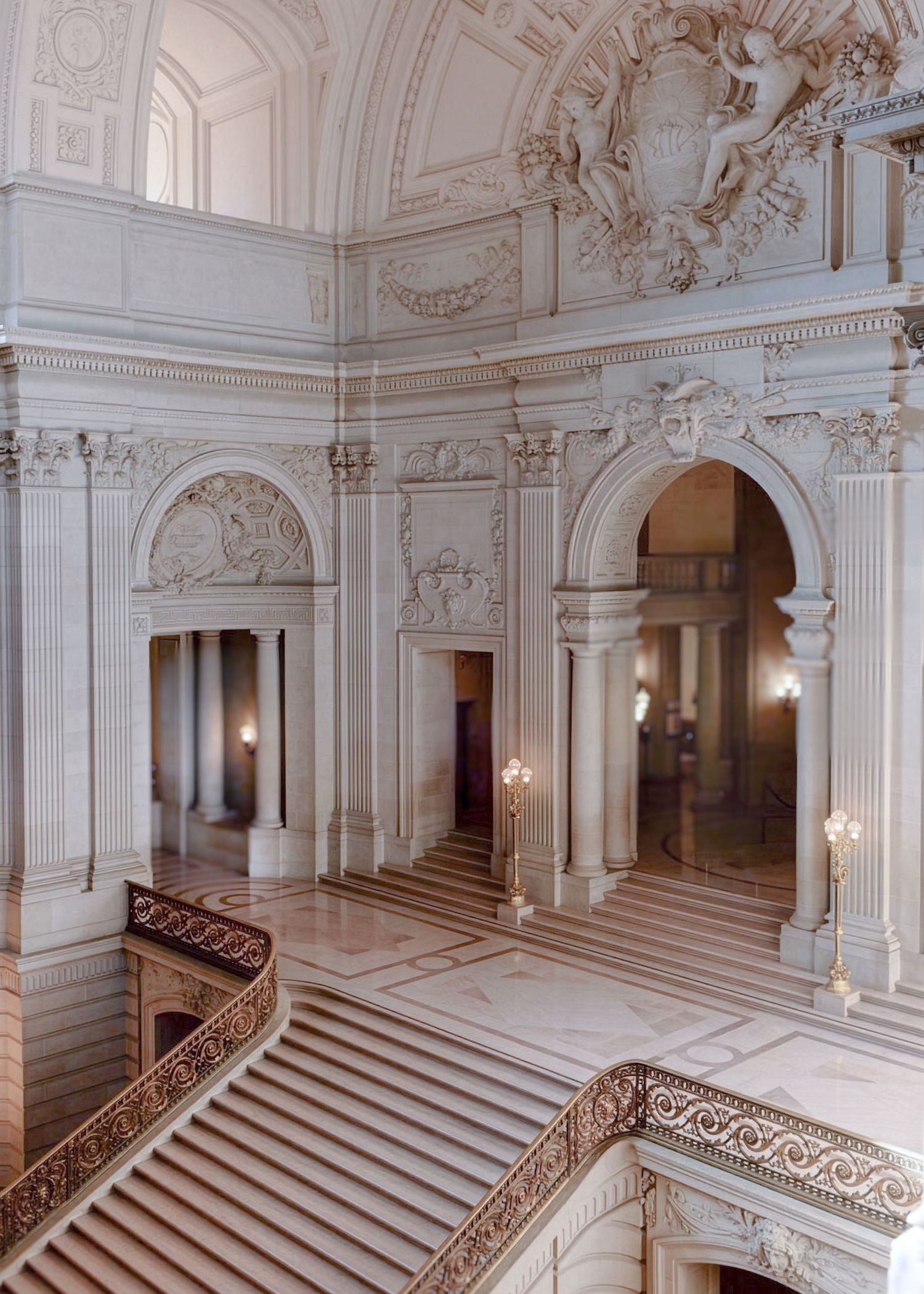 Grand marble staircase inside a Beaux-Arts building with ornate columns, arches, and sculptural details.