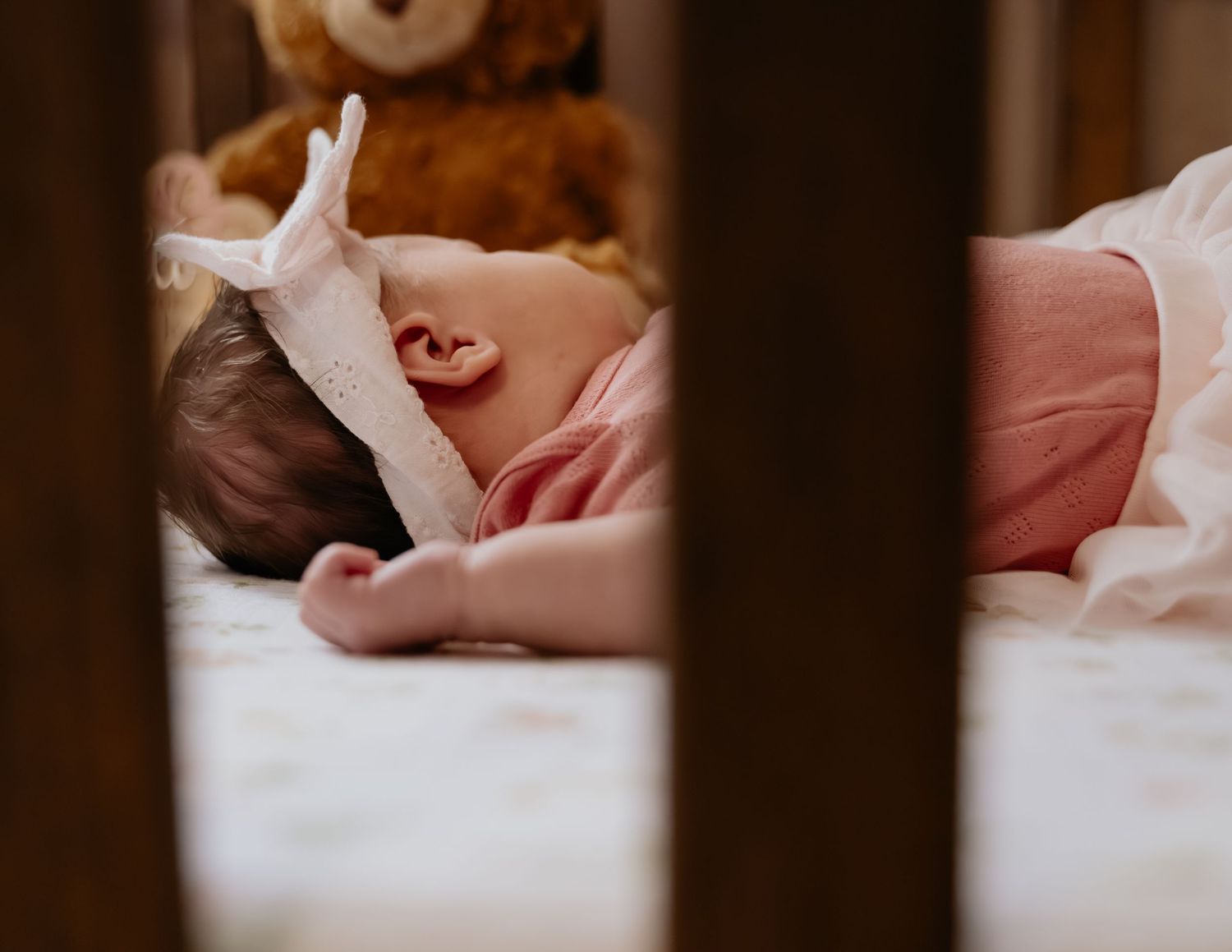 Newborn baby sleeping peacefully in a crib with a soft white toy and teddy bear in background, newborn photography near Sacramento, CA