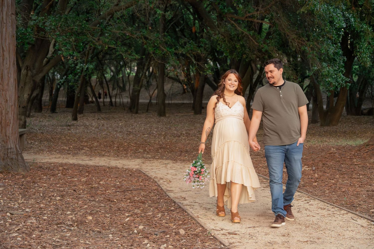 A couple walks hand in hand through a wooded path during a sunny autumn day.