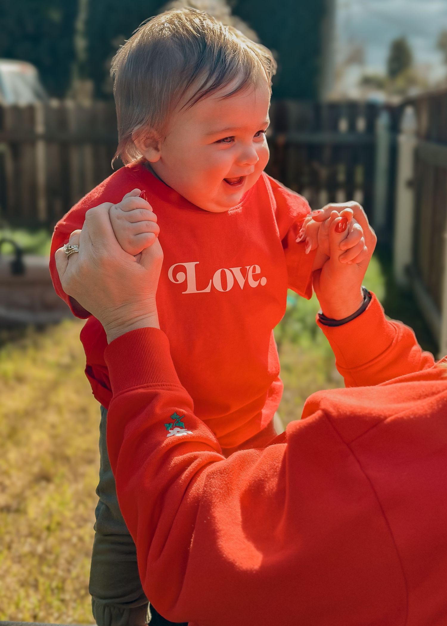 A laughing baby in a bright red 'Love' sweatshirt reaches out with excitement.