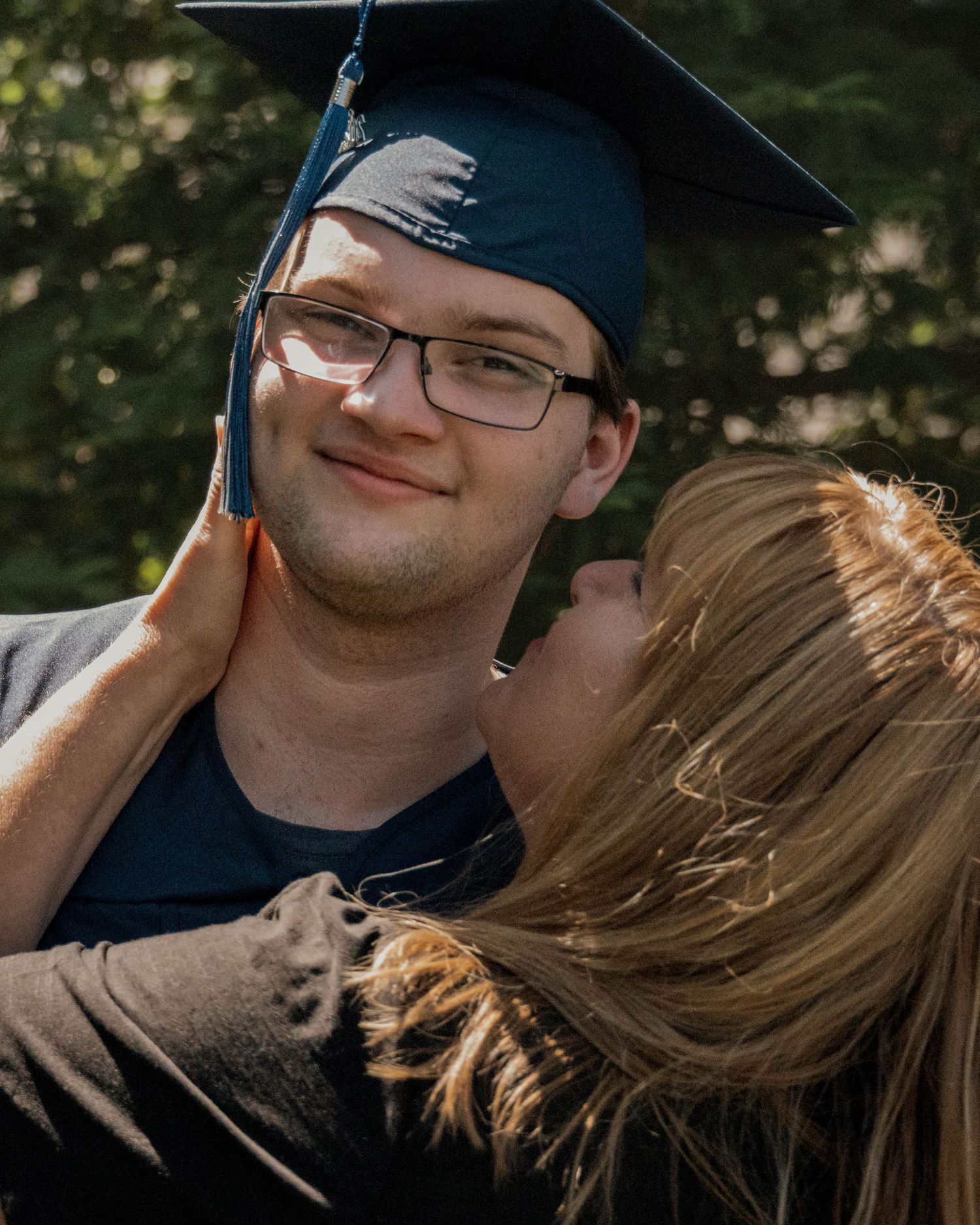 A graduation celebration moment captured outdoors with a cap and gown against a natural background.