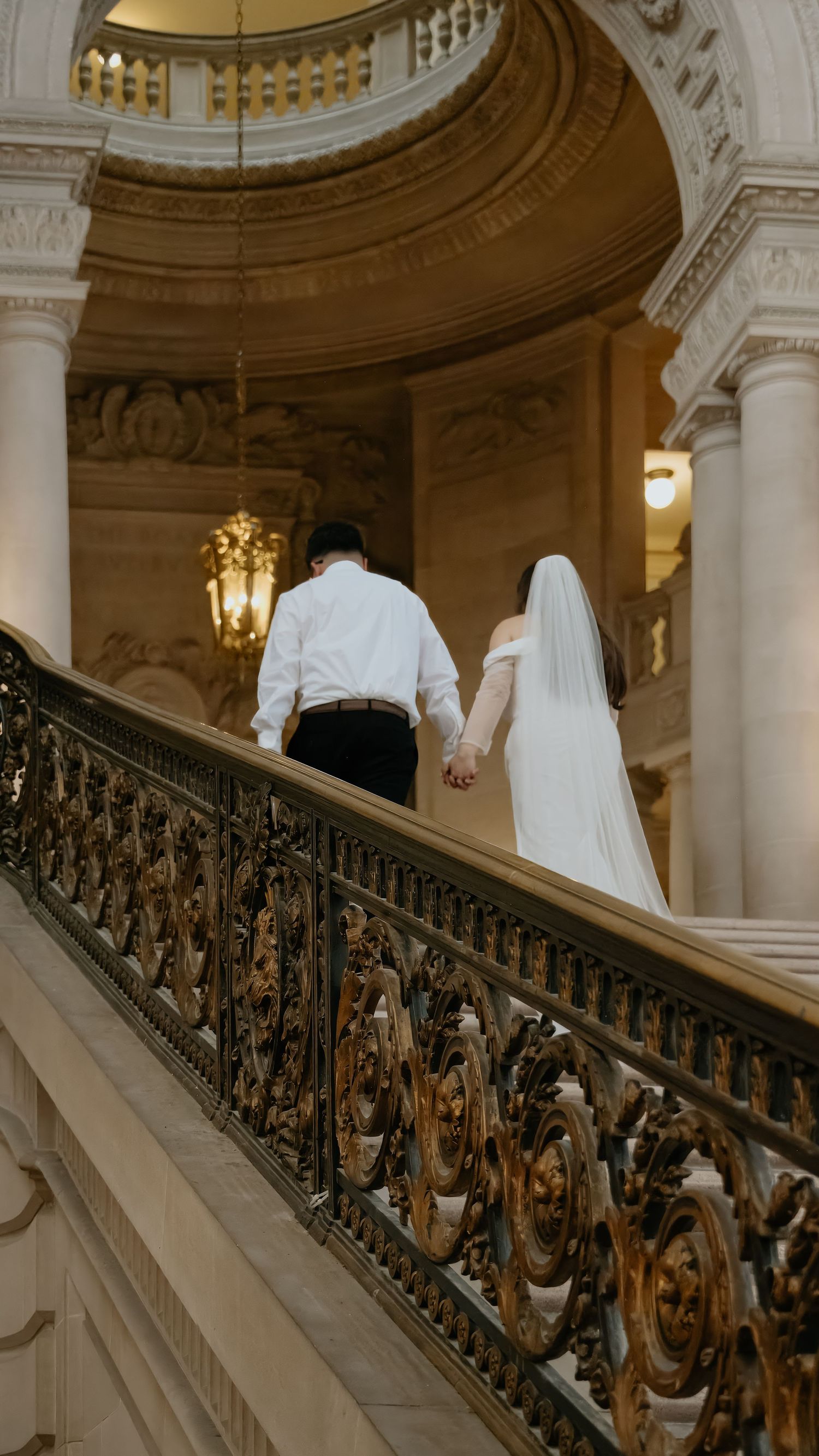 Bride and groom holding hands walking up a grand staircase in elegant San Francisco city hall in small wedding photogrpahy.