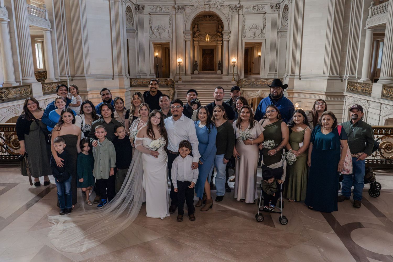 Large wedding party poses together on grand staircase inside San Francisco City Hall.