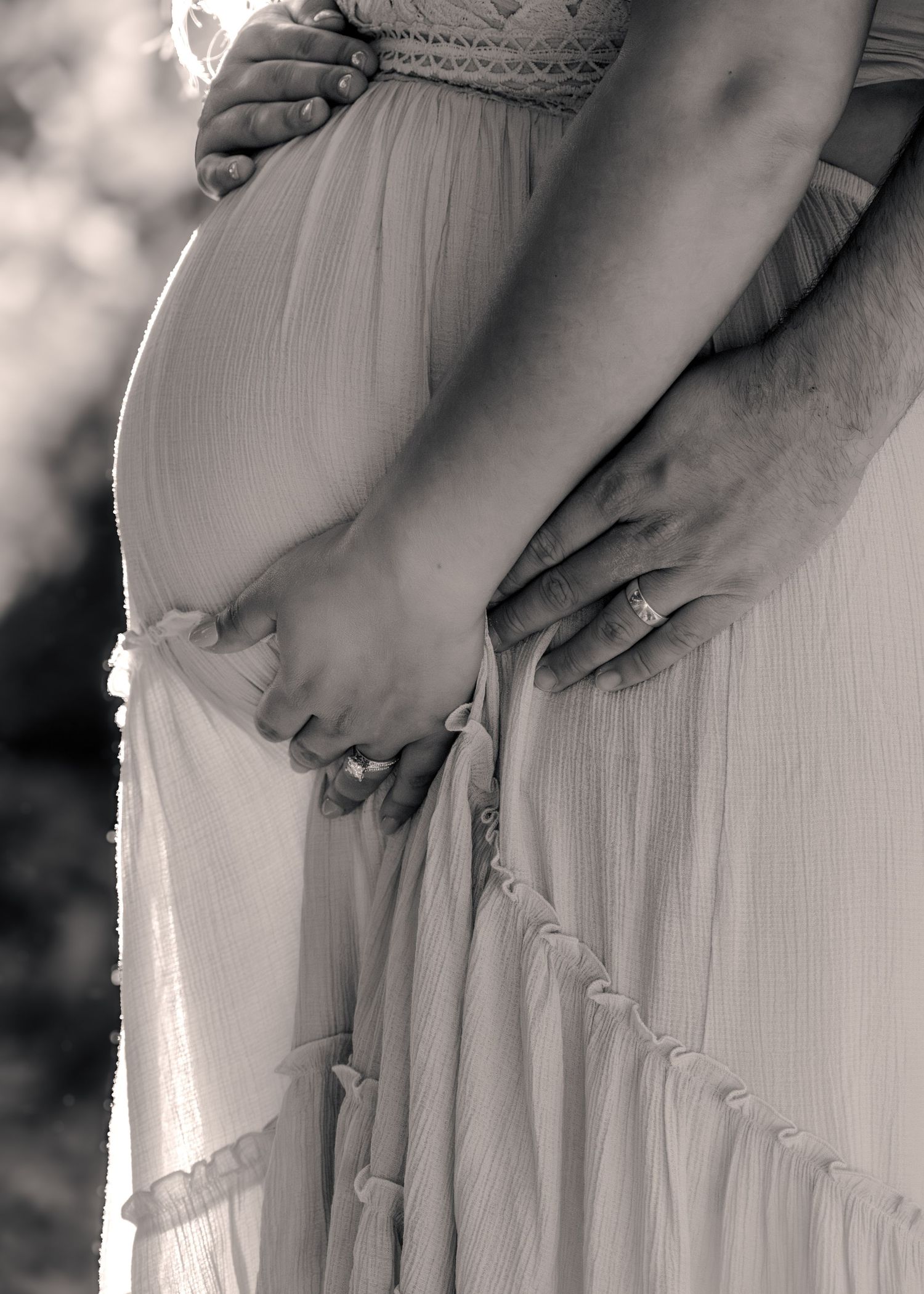 Black and white maternity photo of pregnant woman in flowing dress holding hands with partner outdoors. Rocklin, CA