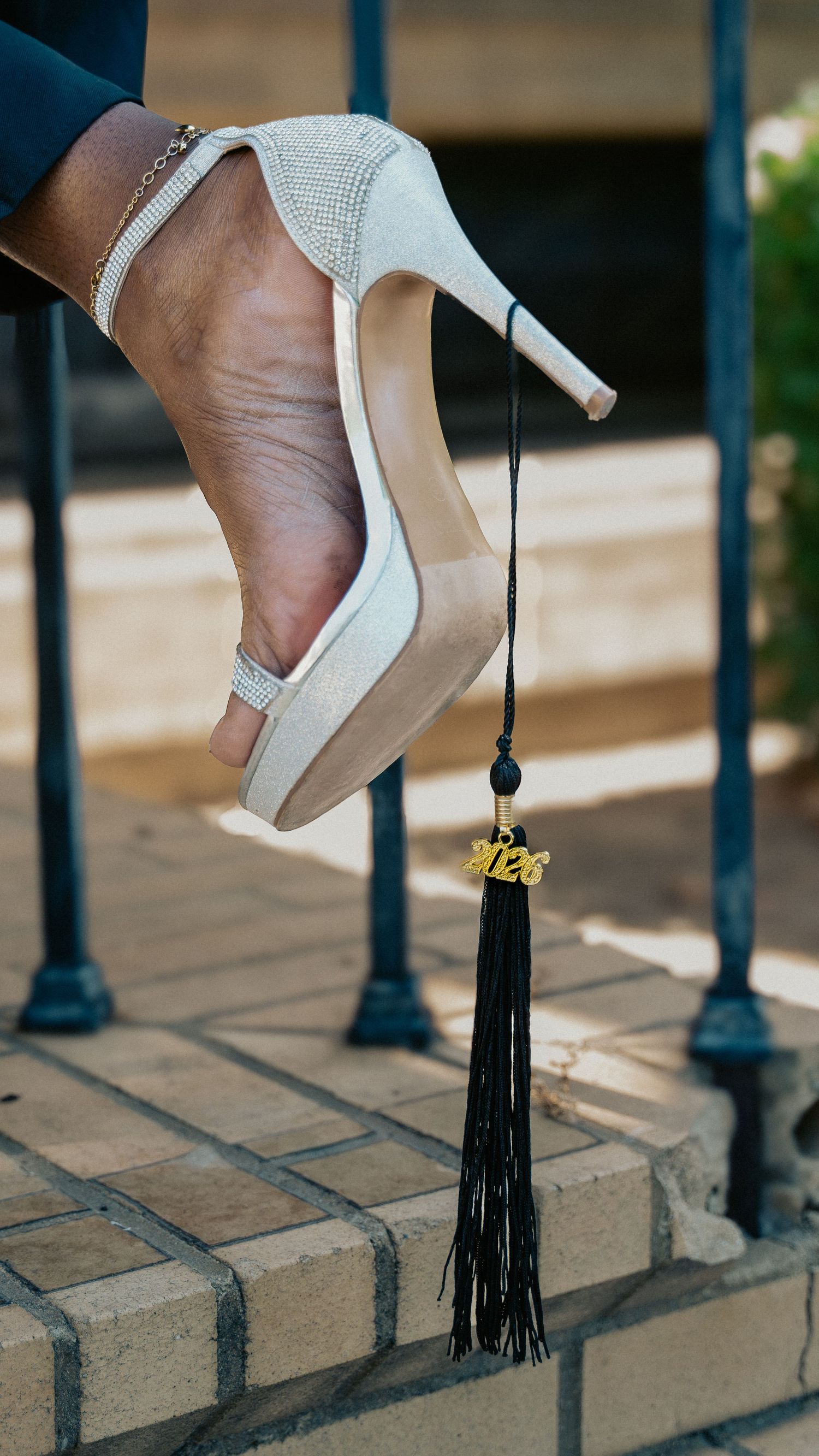 Close-up of a sparkly white stiletto heel with a 2026 graduation tassel hanging from it on brick steps.