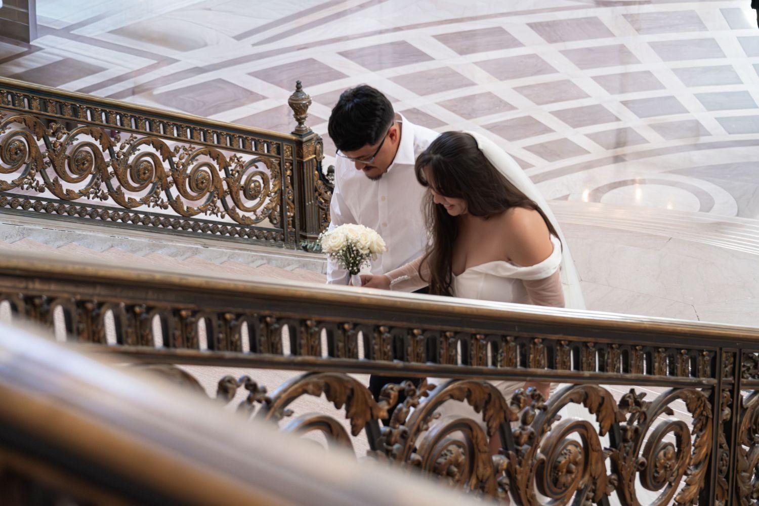 Bride and groom sharing a romantic moment on ornate staircase railing at San Francisco City Hall wedding.