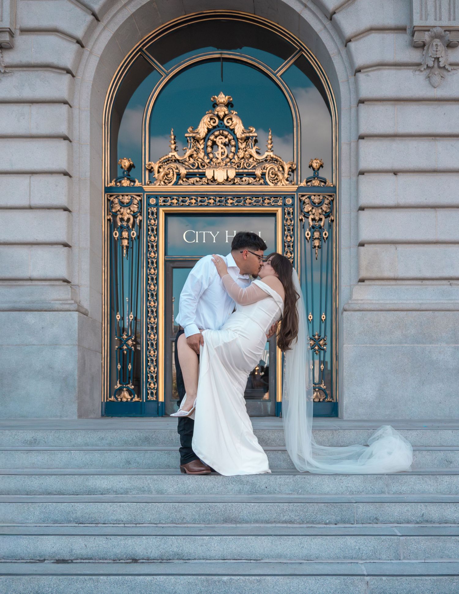 Couple sharing a romantic dip kiss on the steps of San Francisco City Hall in wedding attire.