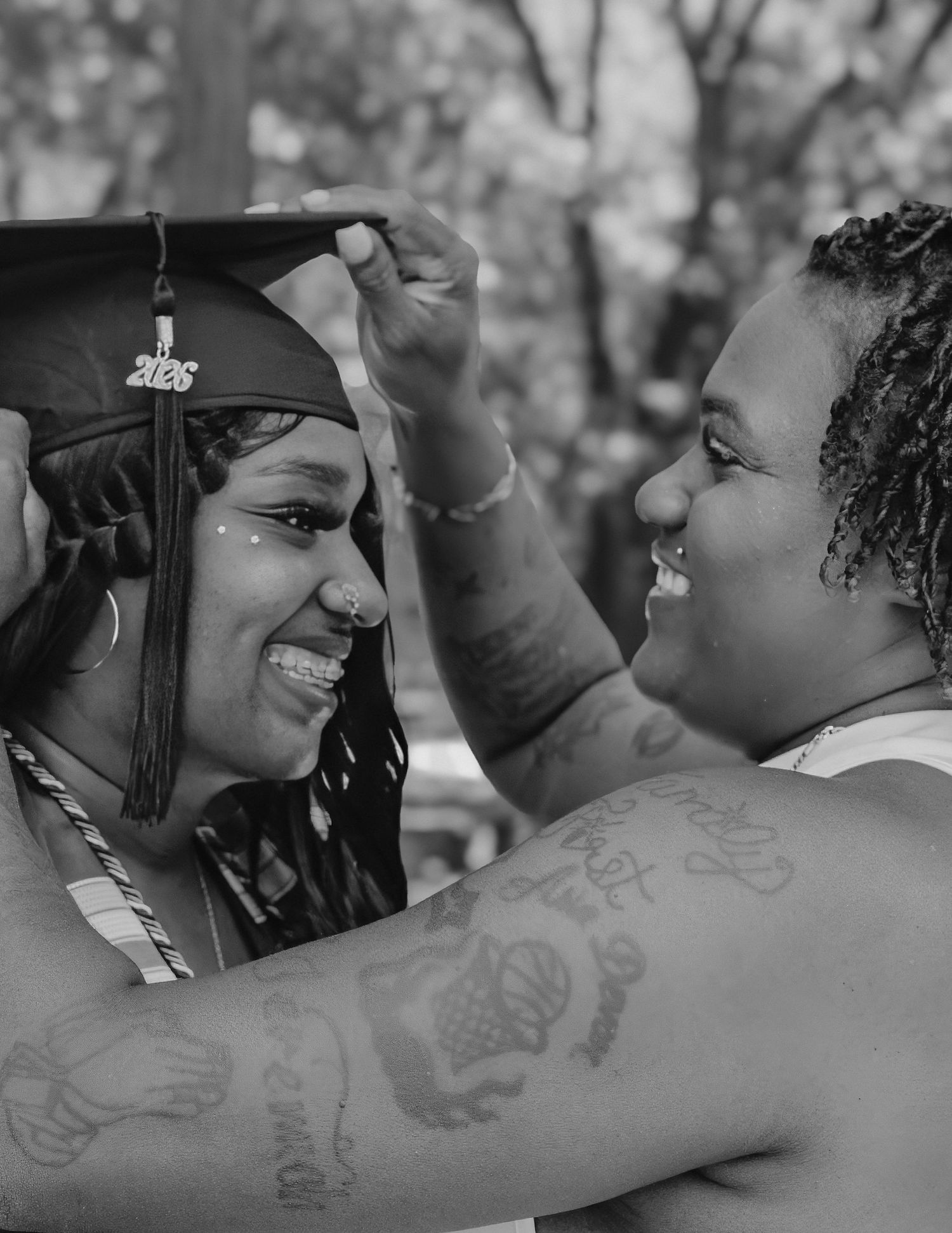 Black and white photo of a graduate smiling as someone adjusts her cap during a graduation ceremony.