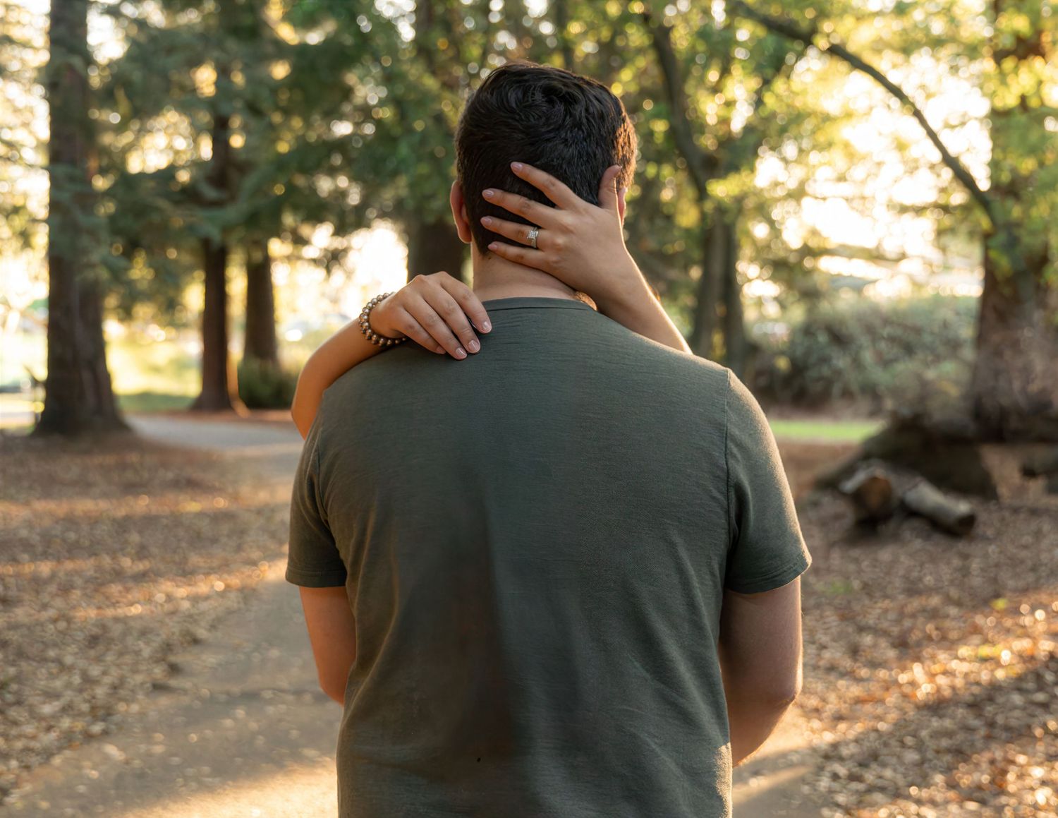 Couple embracing in a sunlit park, man in green shirt with partner's arm around his neck.