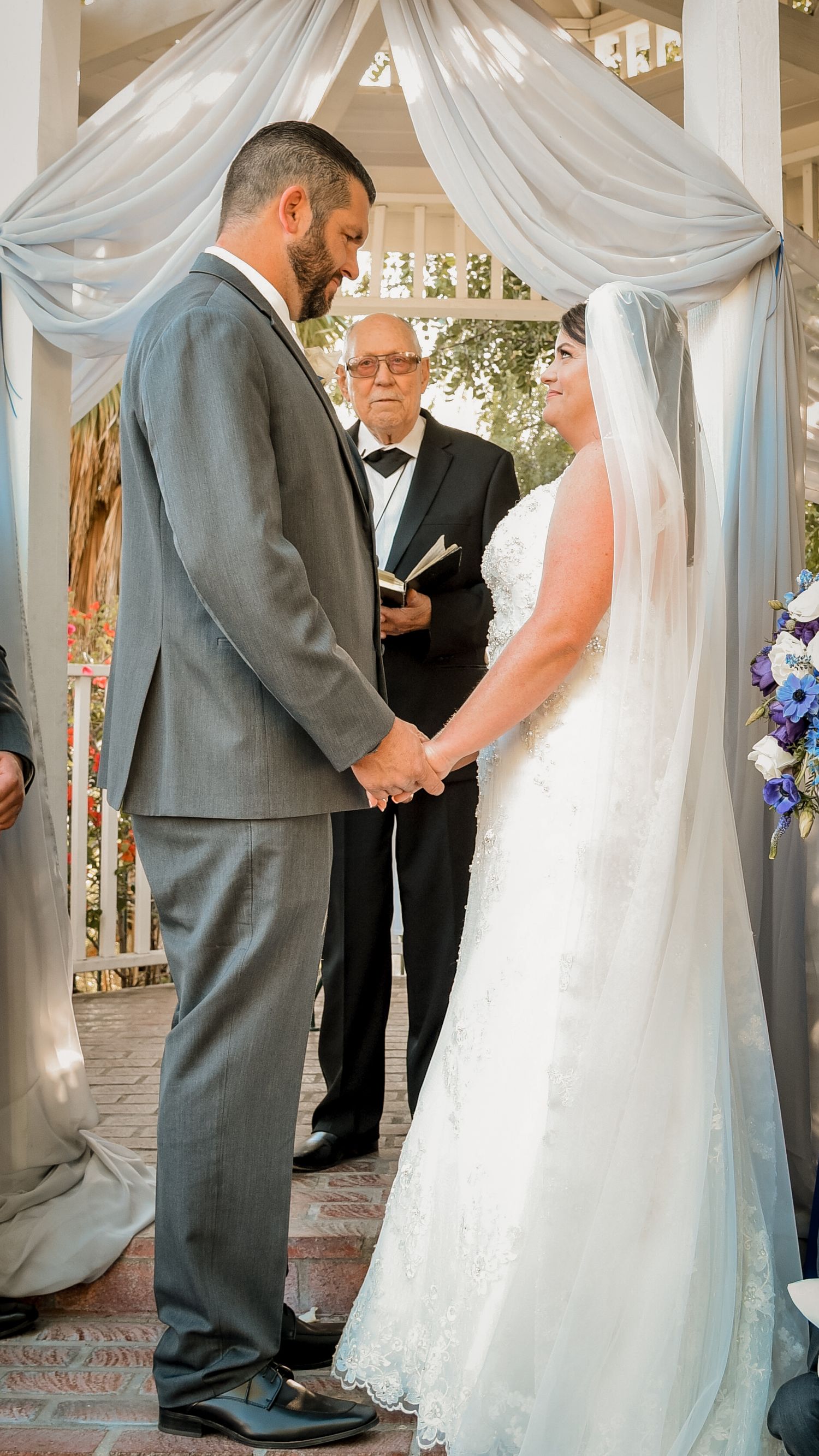 Wedding ceremony taking place under a white draped gazebo with formal attire.
