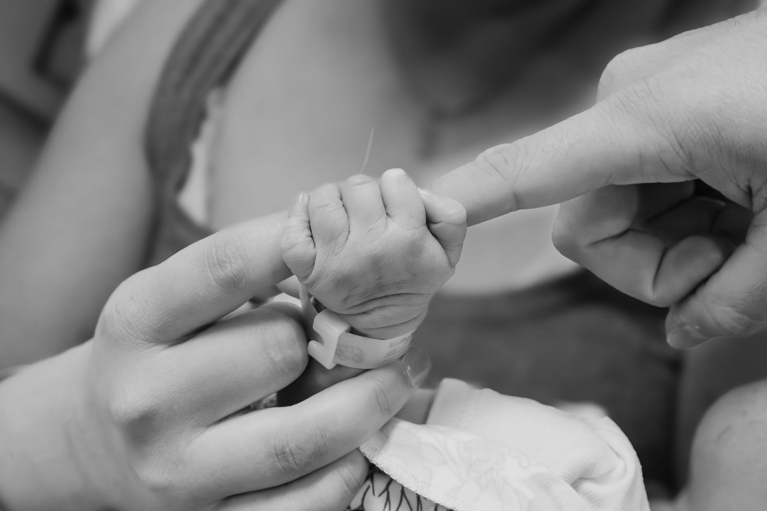 Black and white photo of a newborn baby grasping an adult's finger with tiny hands. Fresh48 photoshoot in hospital, Folsom CA