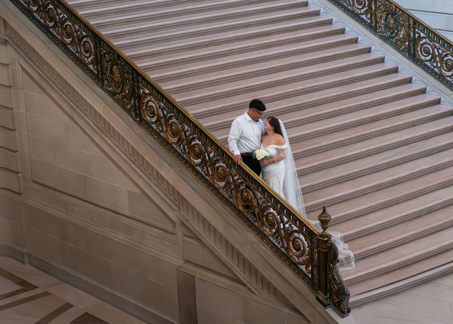 Bride and groom share a romantic moment on grand staircase at San Francisco City Hall wedding.