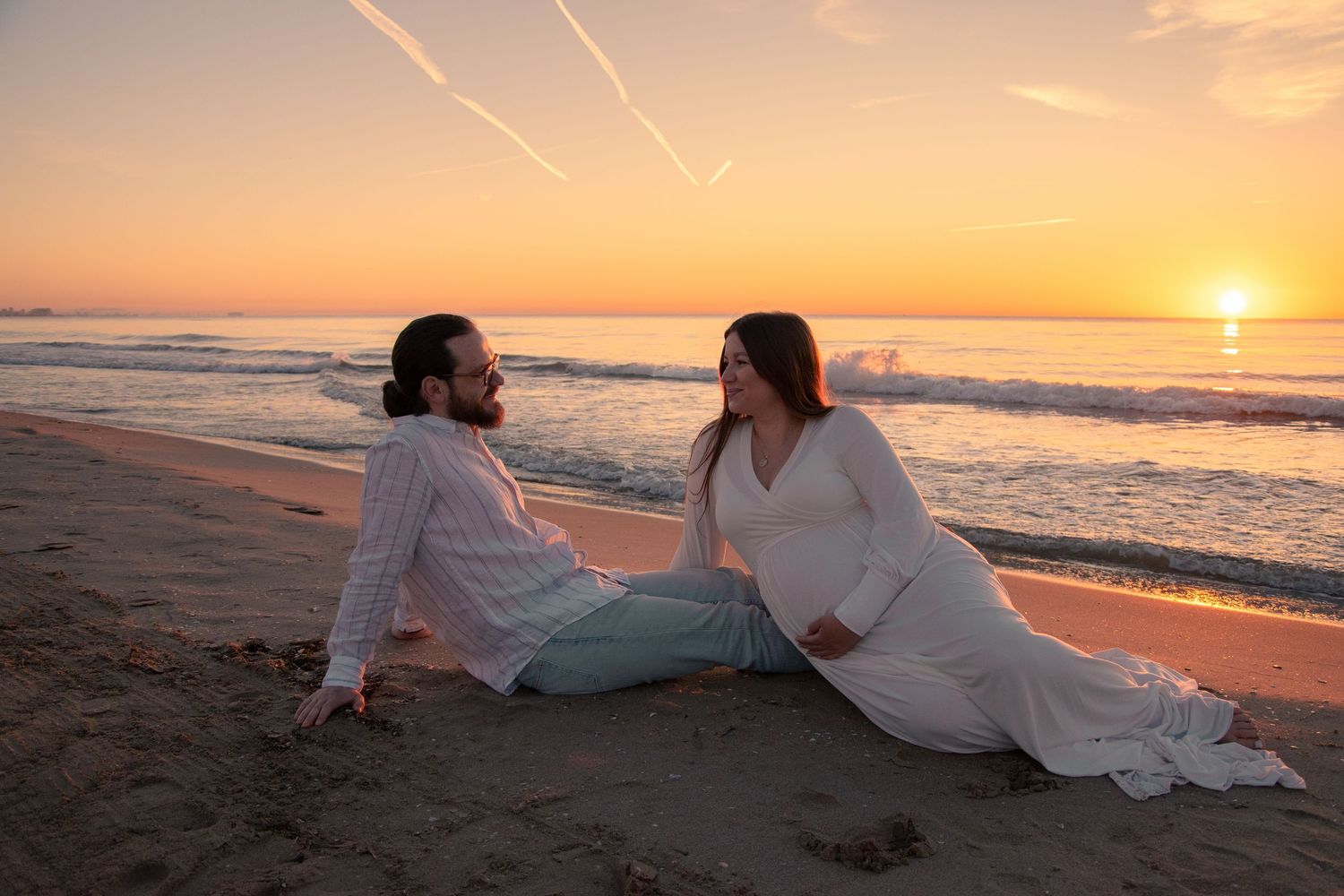Couple relaxes on sandy beach during vibrant orange sunset.