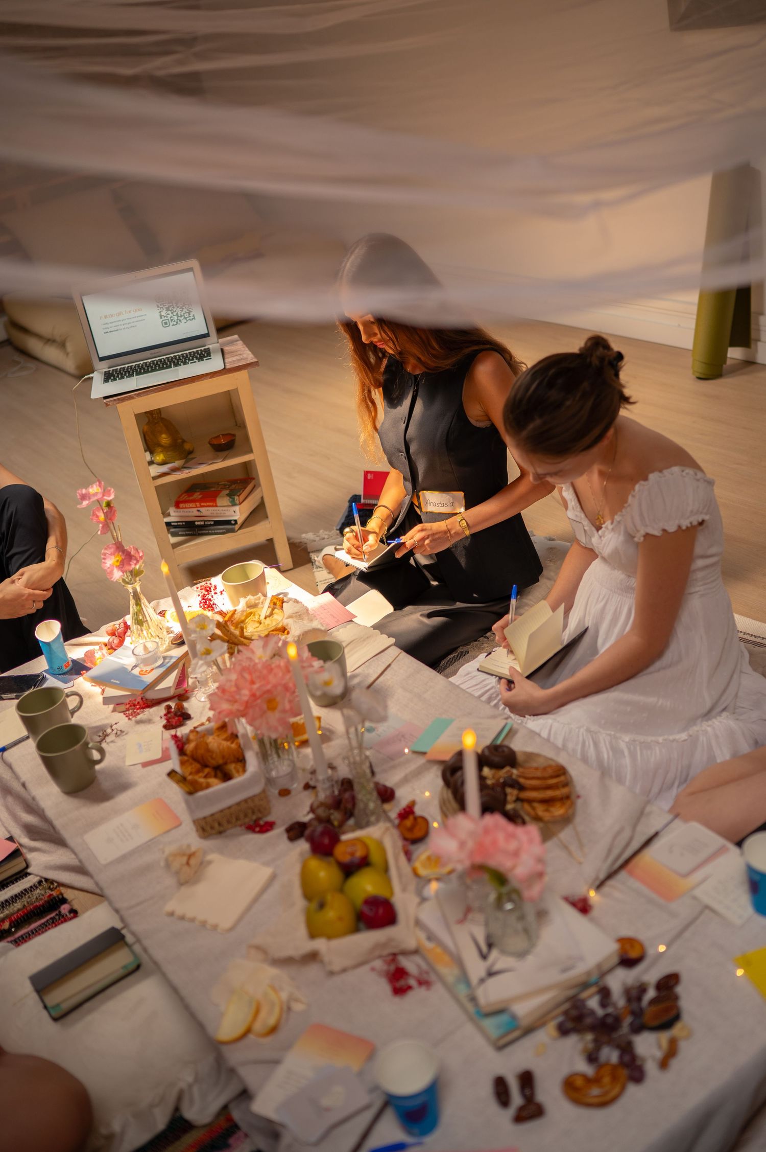 A cozy indoor gathering with people seated around a table filled with food and decorations.