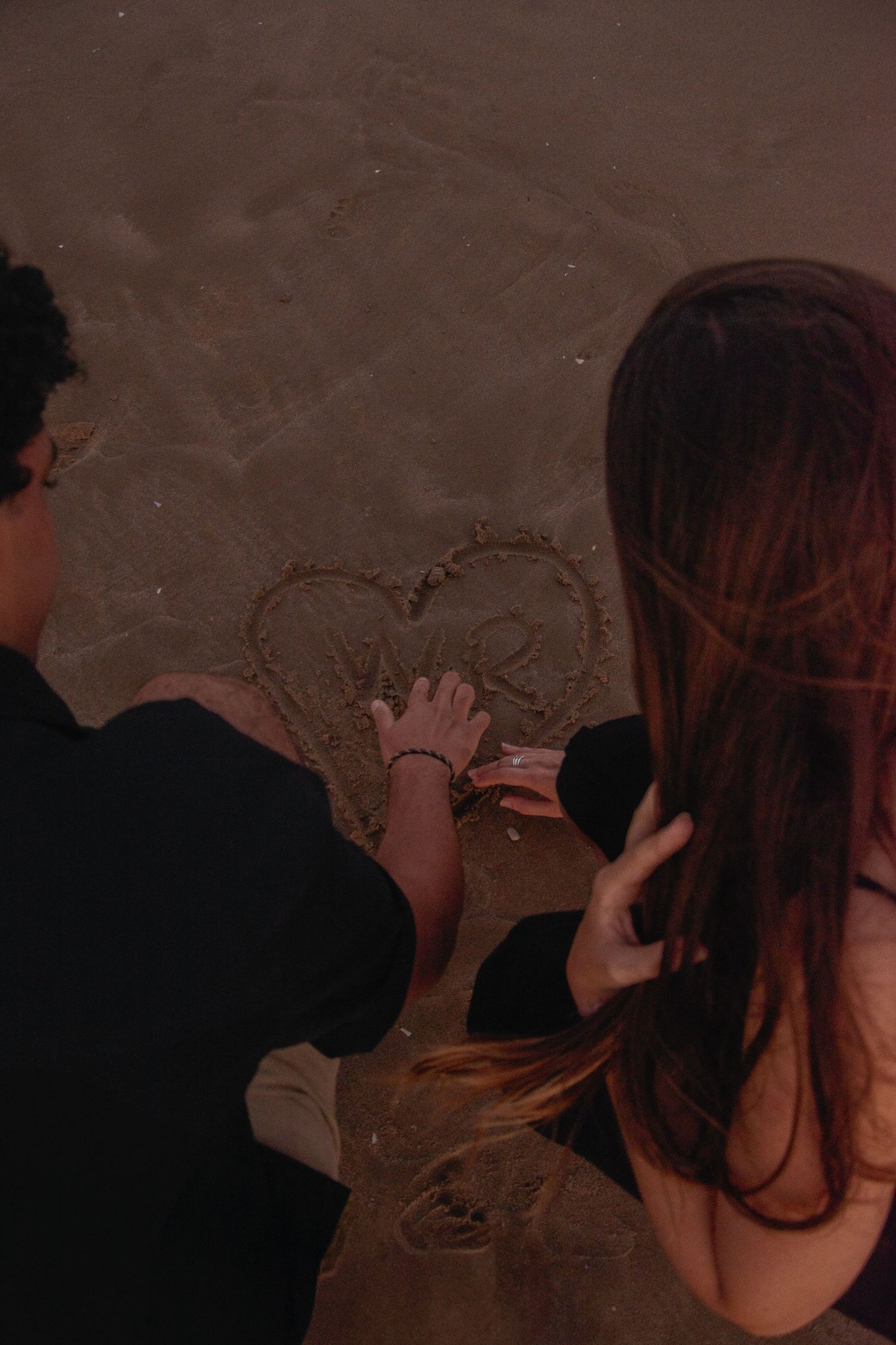 Couple writes in the sand on a beach during sunset.