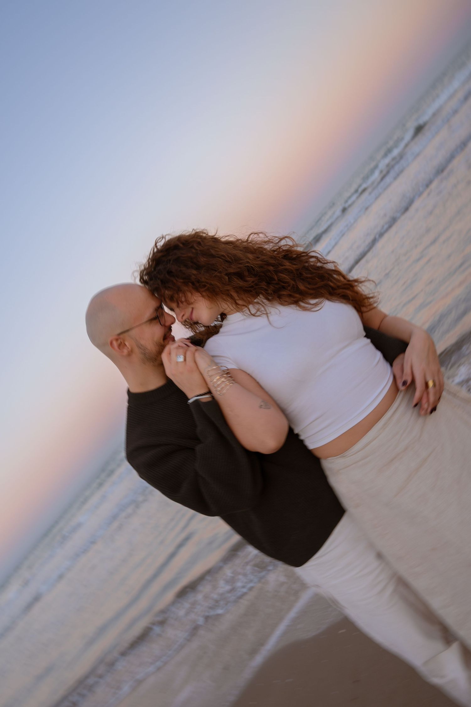 Couple embracing on a beach during golden hour with ocean waves in background.