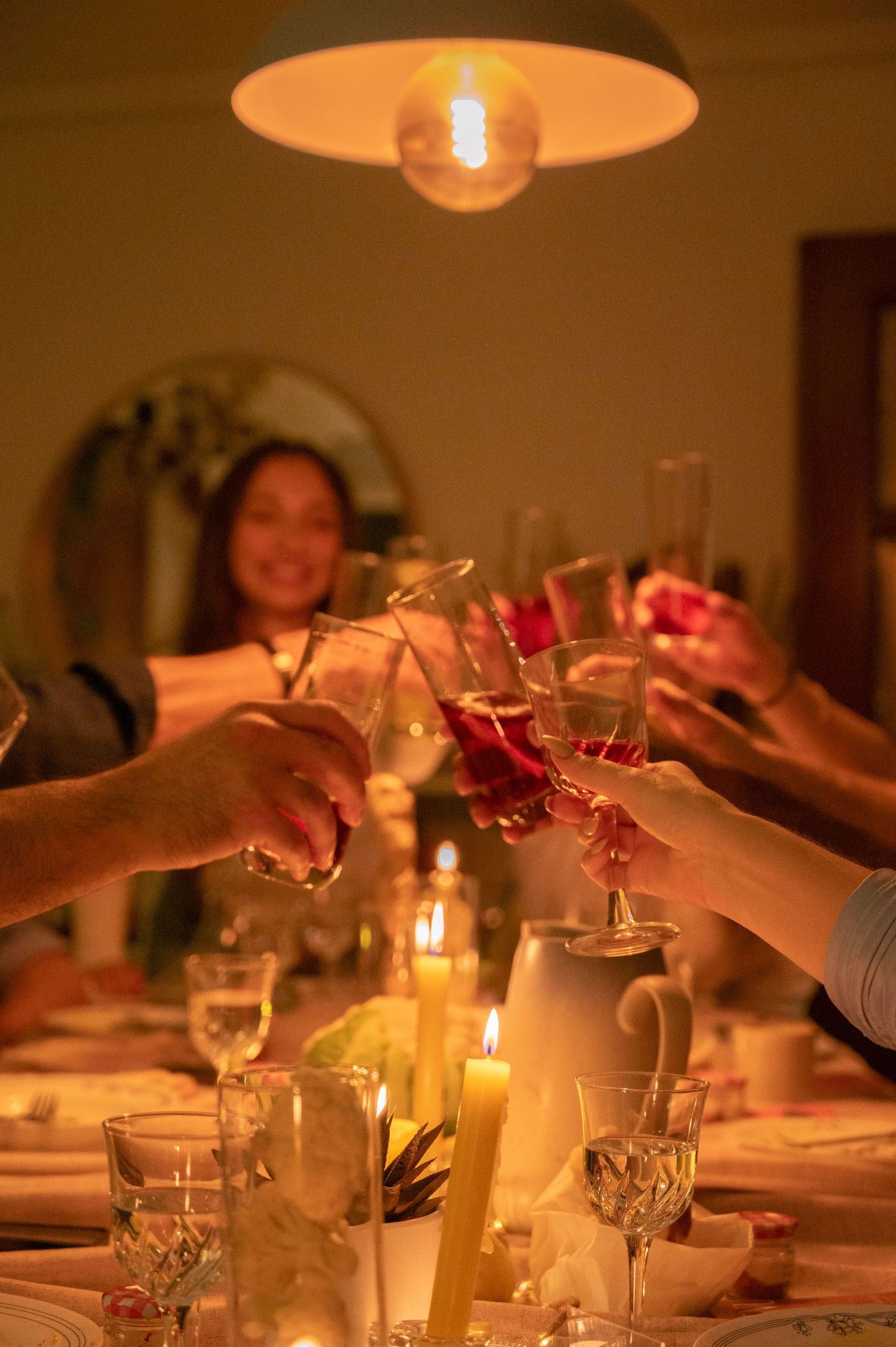 Hands raising glasses in a toast during a candlelit dinner party.